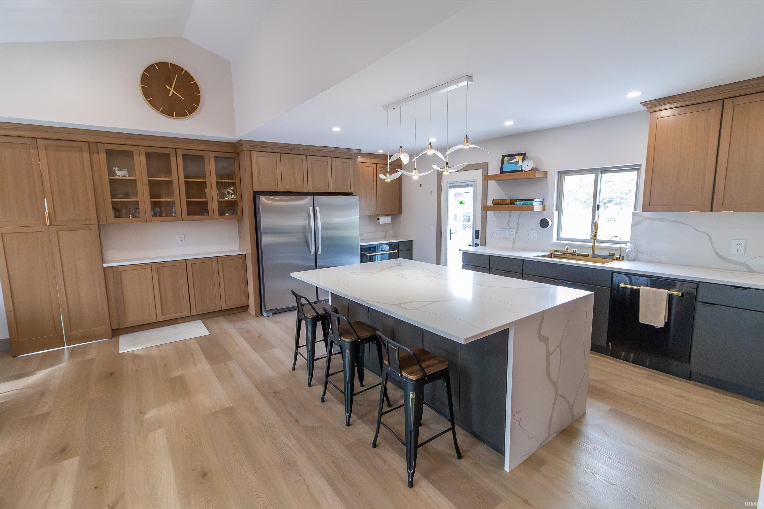 Dual tone kitchen featuring stainless steel appliances, light stone countertops, a kitchen bar, open shelves, and two tone cabinetry