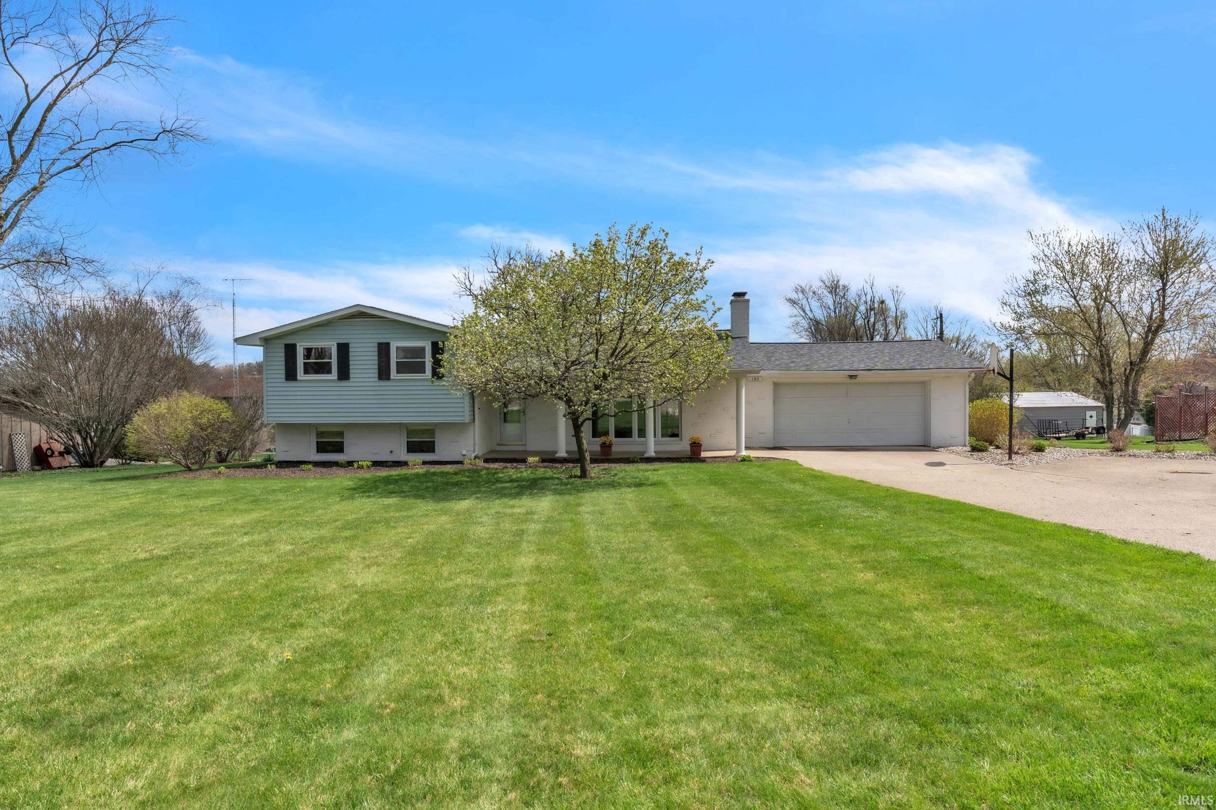 Split level home featuring an attached garage, concrete driveway, a front yard, and a chimney
