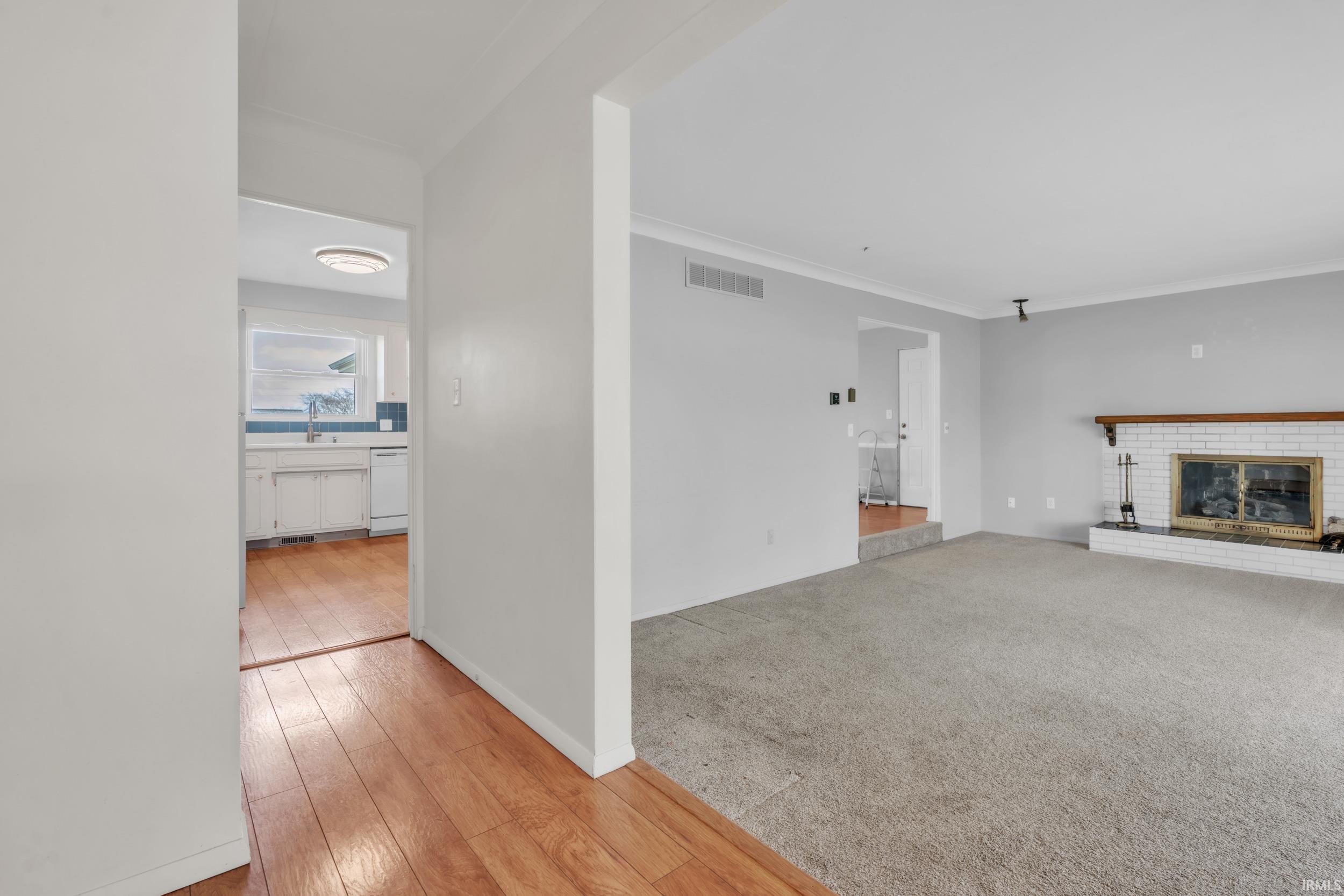 Unfurnished living room featuring a fireplace, light wood-style flooring, crown molding, and light colored carpet