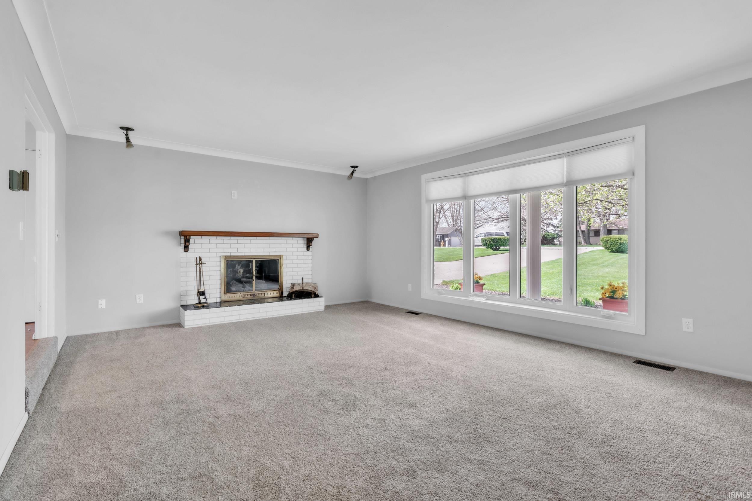 Unfurnished living room with a brick fireplace, carpet flooring, and ornamental molding