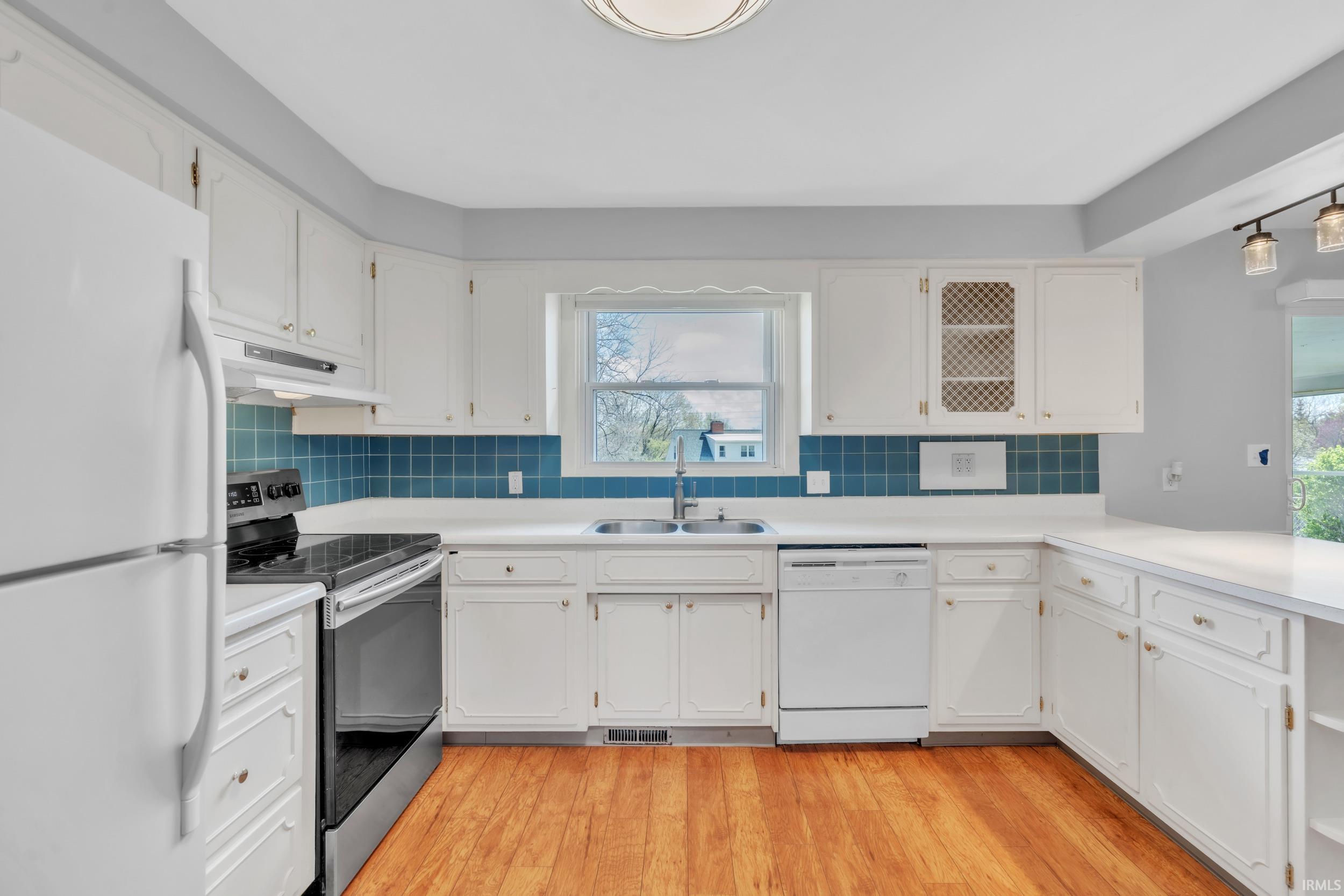 Kitchen with white appliances, light countertops, white cabinets, light wood-style floors, and tasteful backsplash