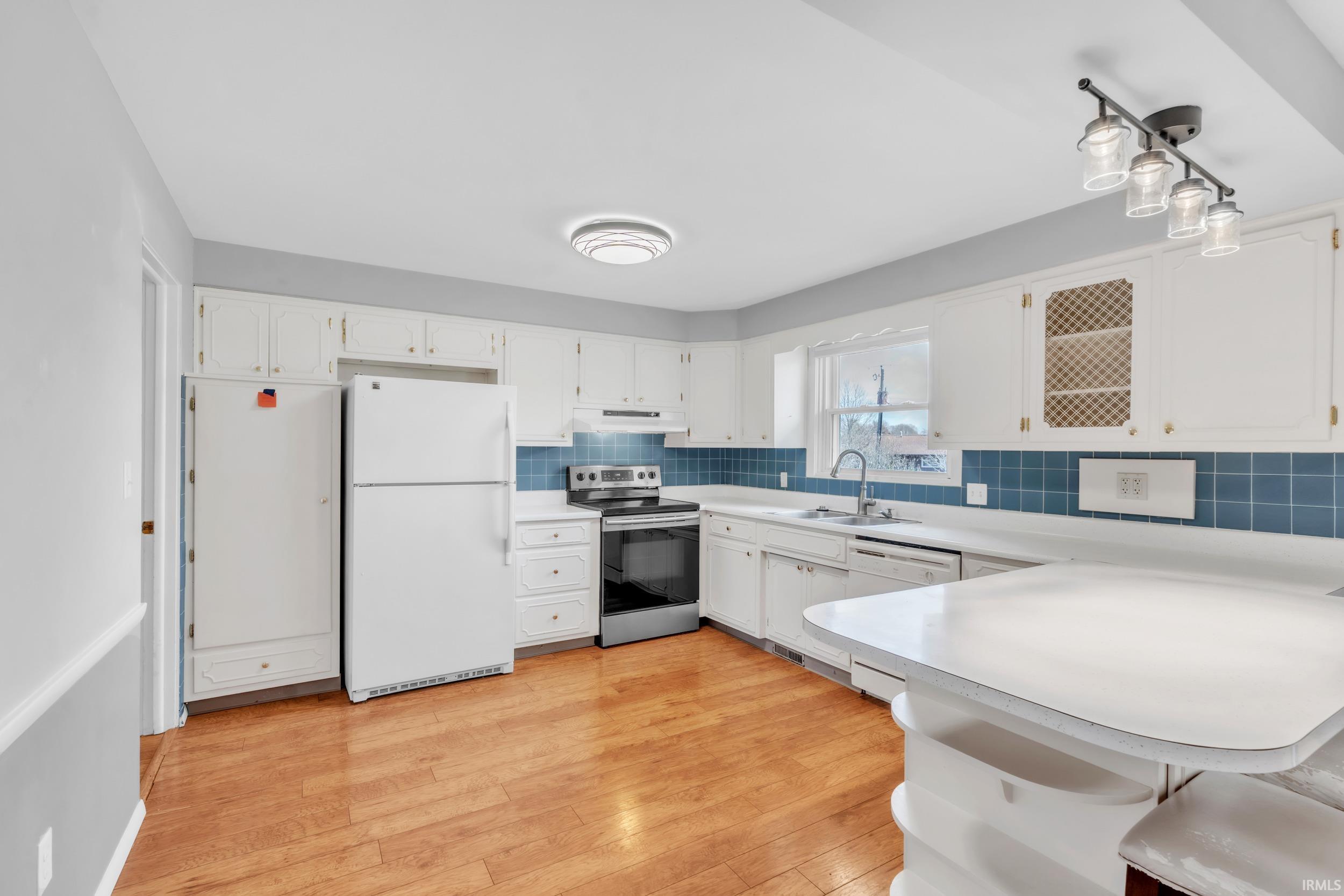 Kitchen with a peninsula, white appliances, light countertops, white cabinetry, and a kitchen bar