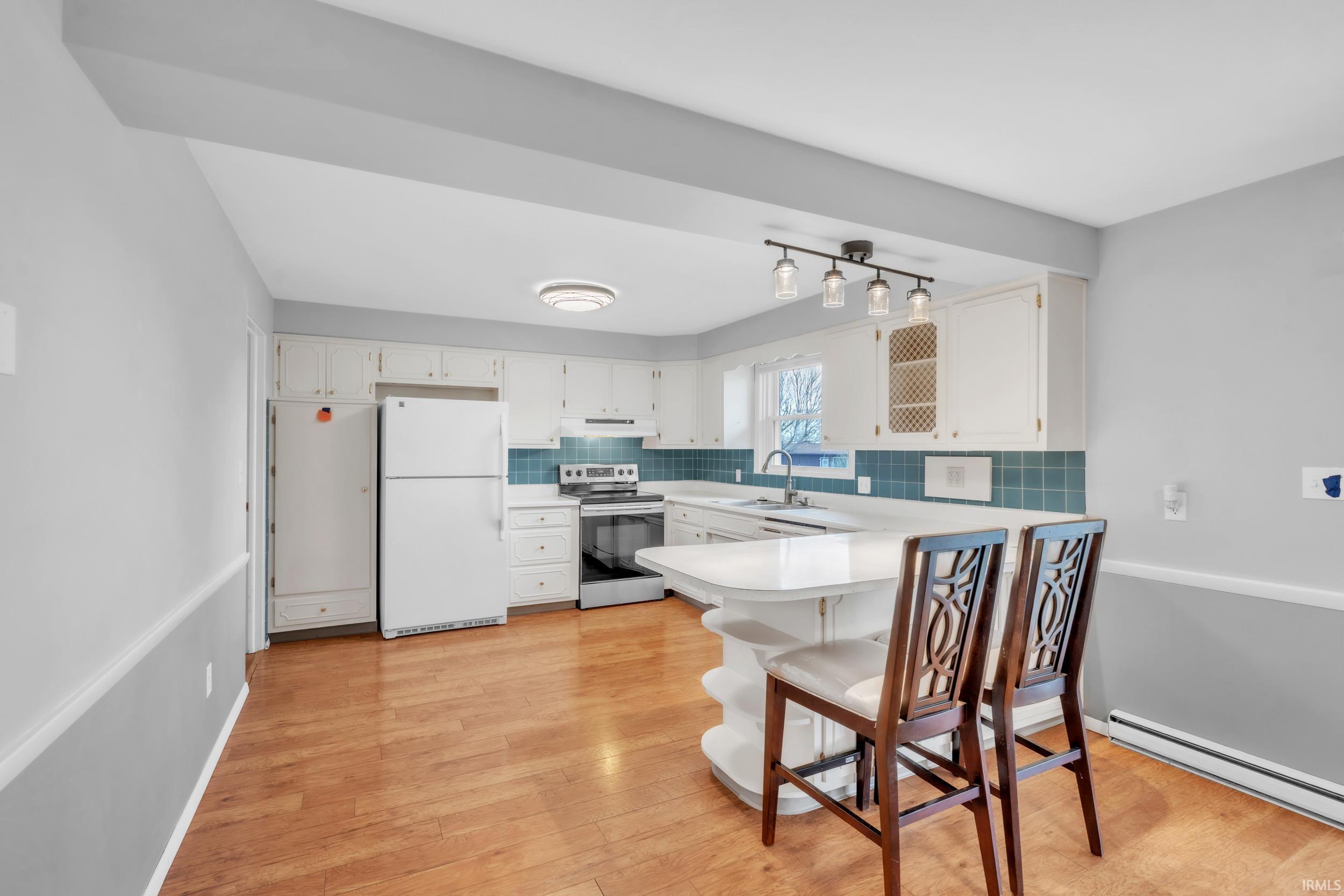 Kitchen featuring light countertops, freestanding refrigerator, electric stove, a peninsula, and light wood finished floors