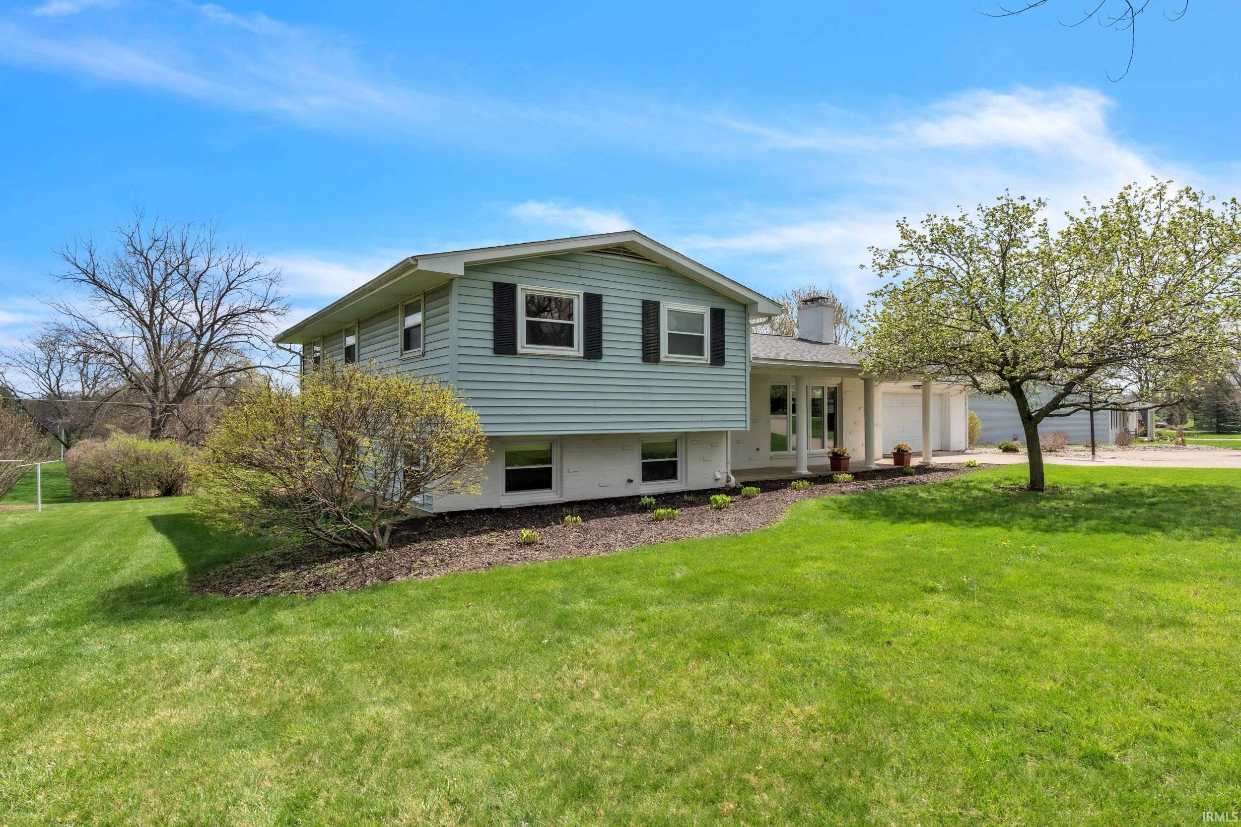 Tri-level home featuring an attached garage, a front lawn, a chimney, concrete driveway, and a porch