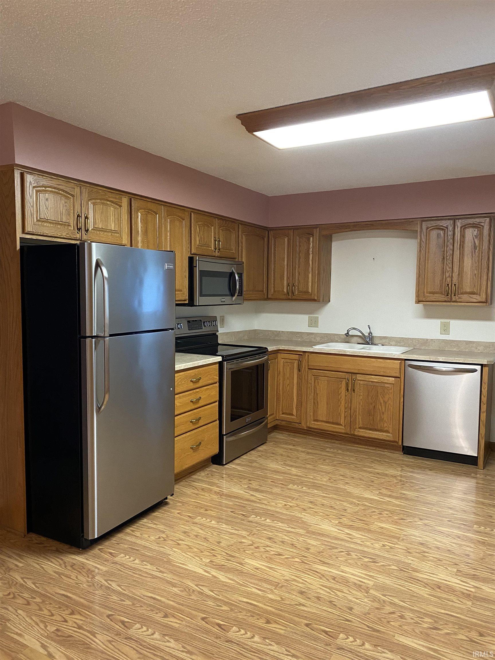 Kitchen with stainless steel appliances, vinyl plank flooring and wood finish cabinetry.