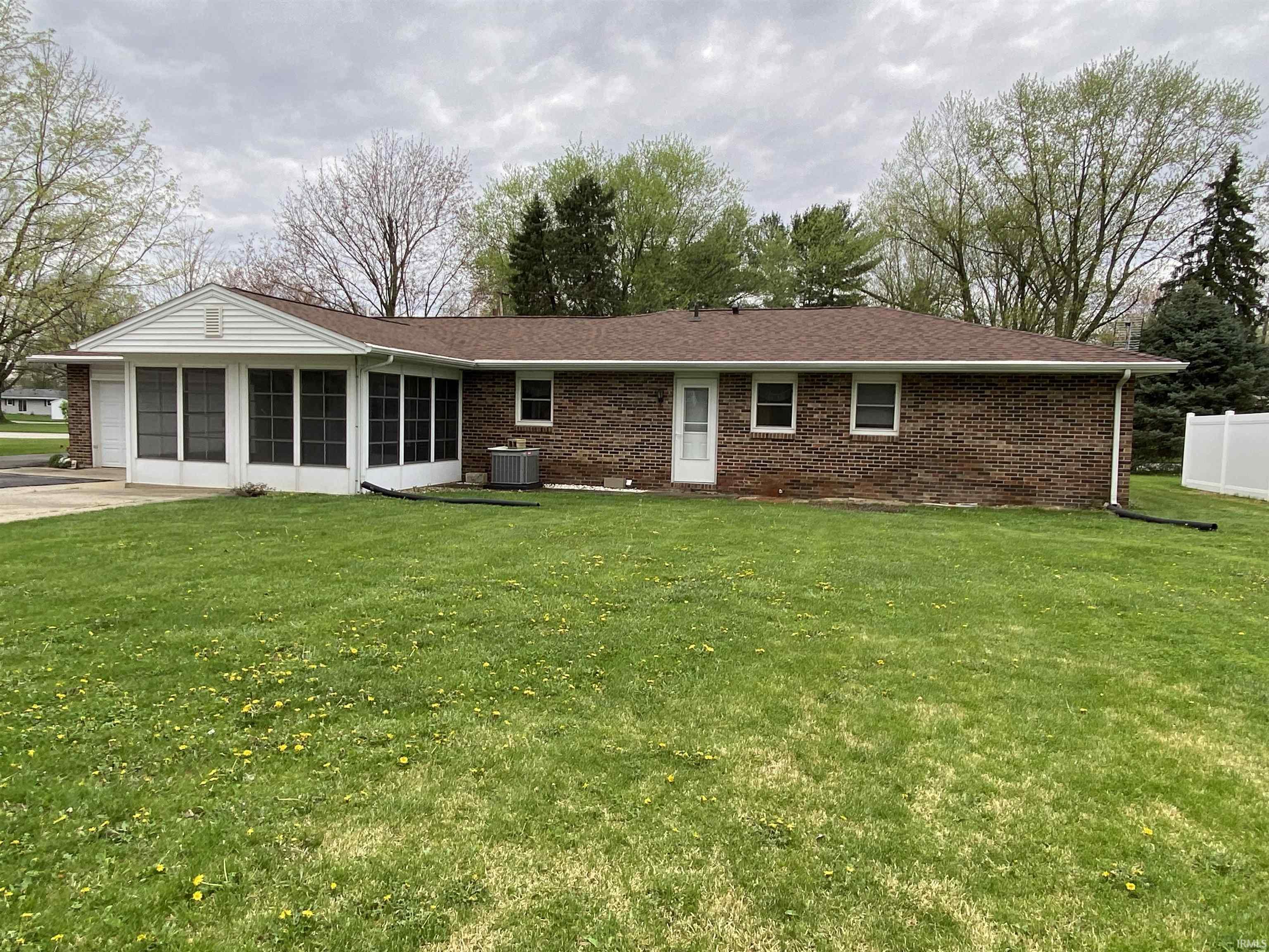 Back of house with a lawn, brick siding, a sun room, and roof with shingles.