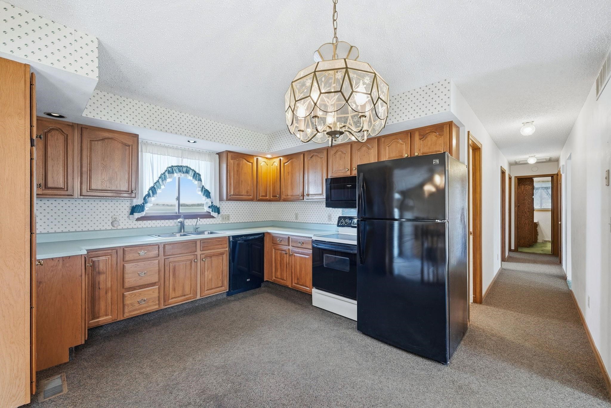Kitchen featuring wood cabinetry, laminate countertops, a double basin sink, and black appliances