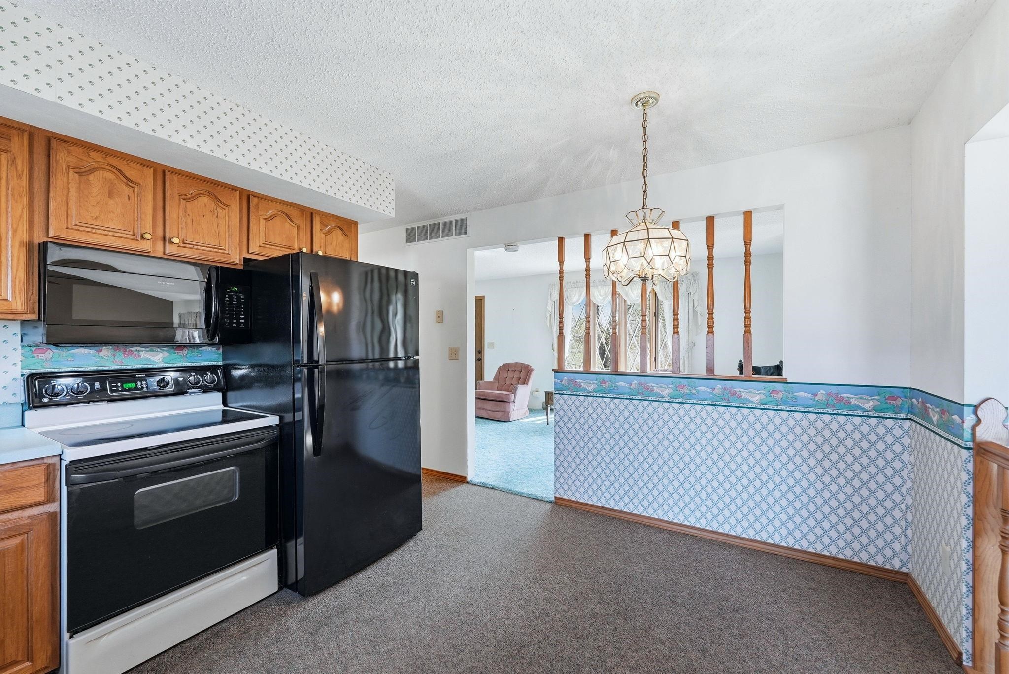 Kitchen featuring wood cabinetry, black appliances, and carpeted flooring