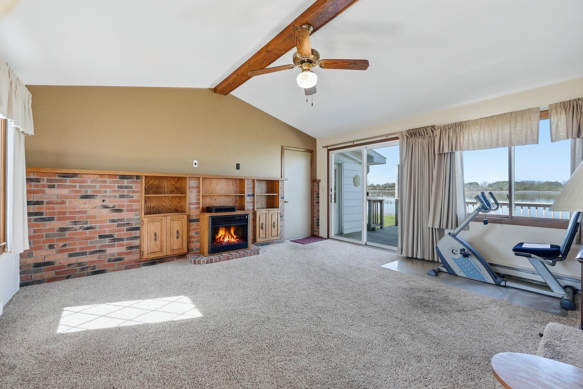 Vaulted ceiling with exposed wood beam, carpeted flooring, brick accent wall with built-in cabinetry, and a fireplace with brick surround