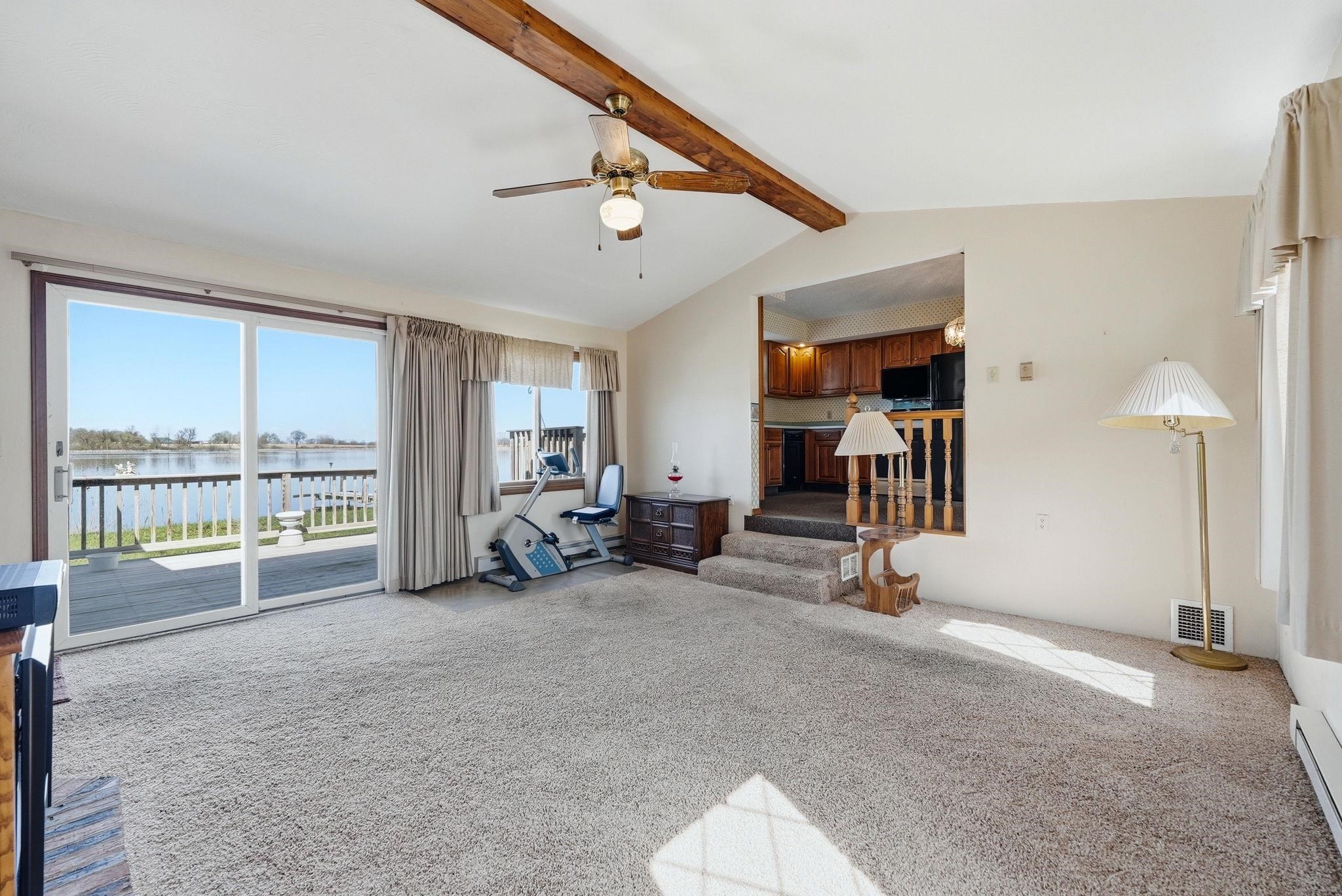 Spacious living area featuring vaulted ceilings with exposed wood beams and a ceiling fan