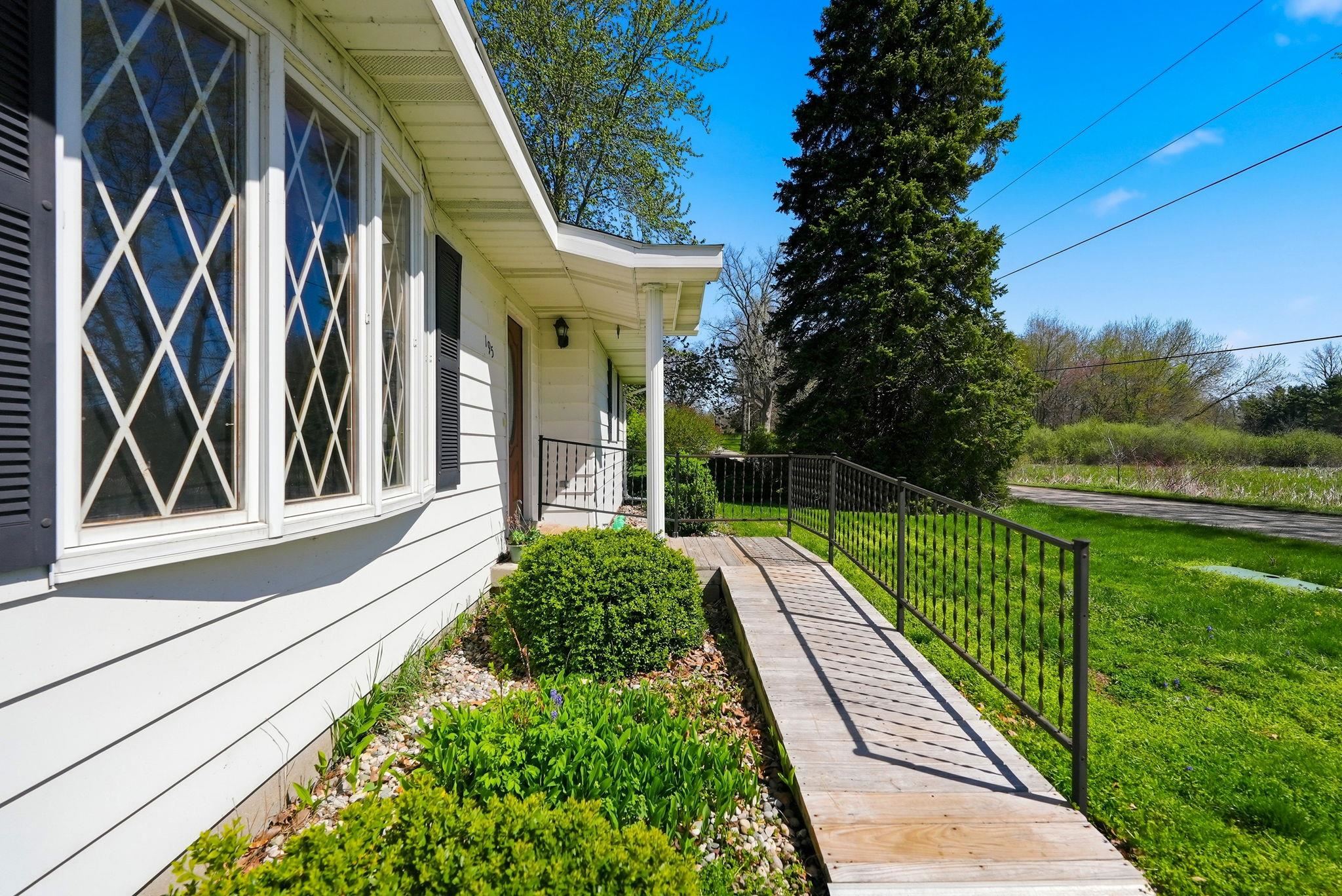 Ranch-style exterior with white siding, bay window featuring diamond-pattern grilles, black louvered shutters, and a covered porch