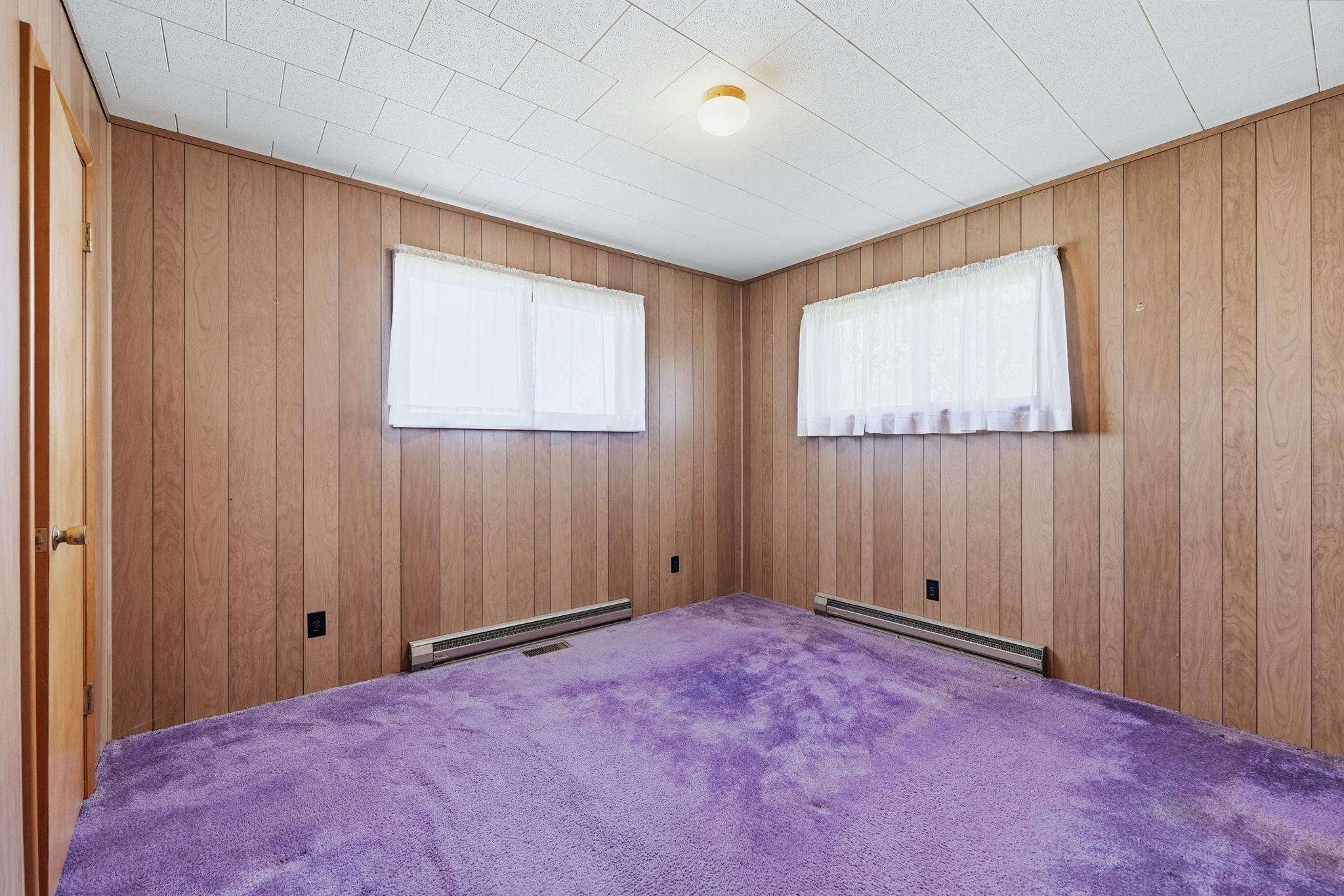 Room featuring wood paneling, purple carpeting, and two windows