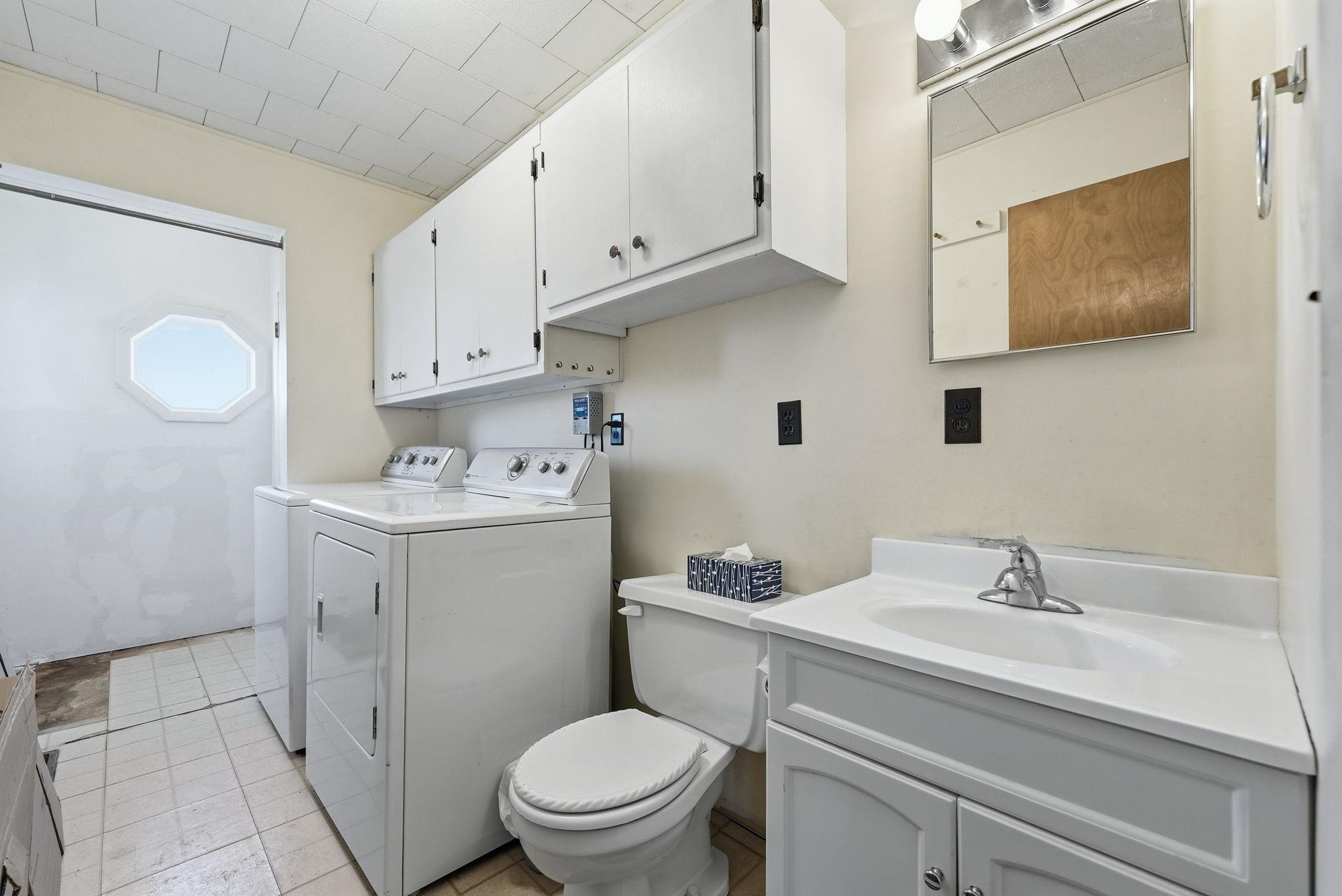 Laundry room featuring a full-size washer and dryer, white cabinetry, tile flooring, a single vanity with an integrated sink, and an octagonal window