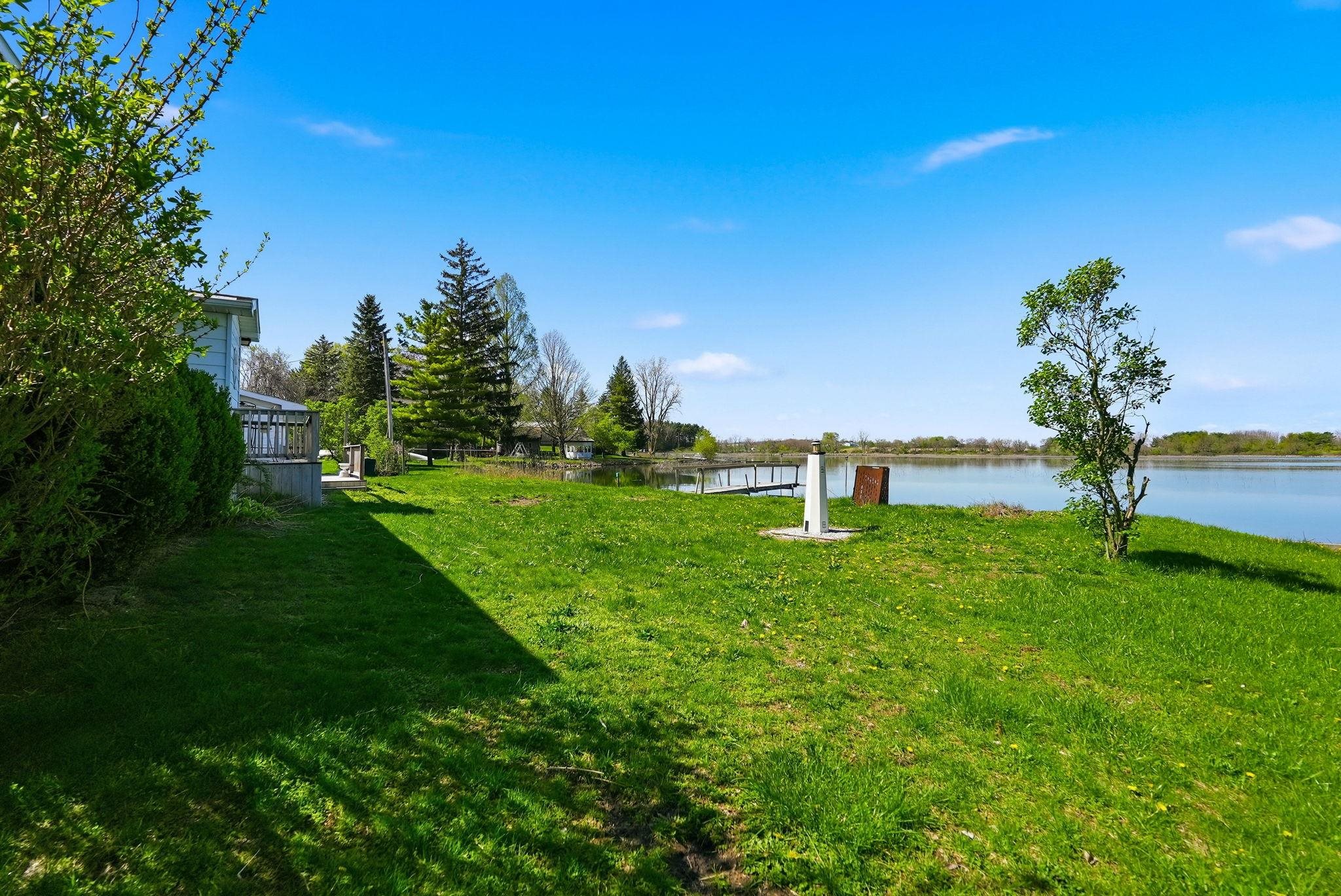 Expansive waterfront property featuring a large grassy area, mature trees, and direct access to the water with a dock structure