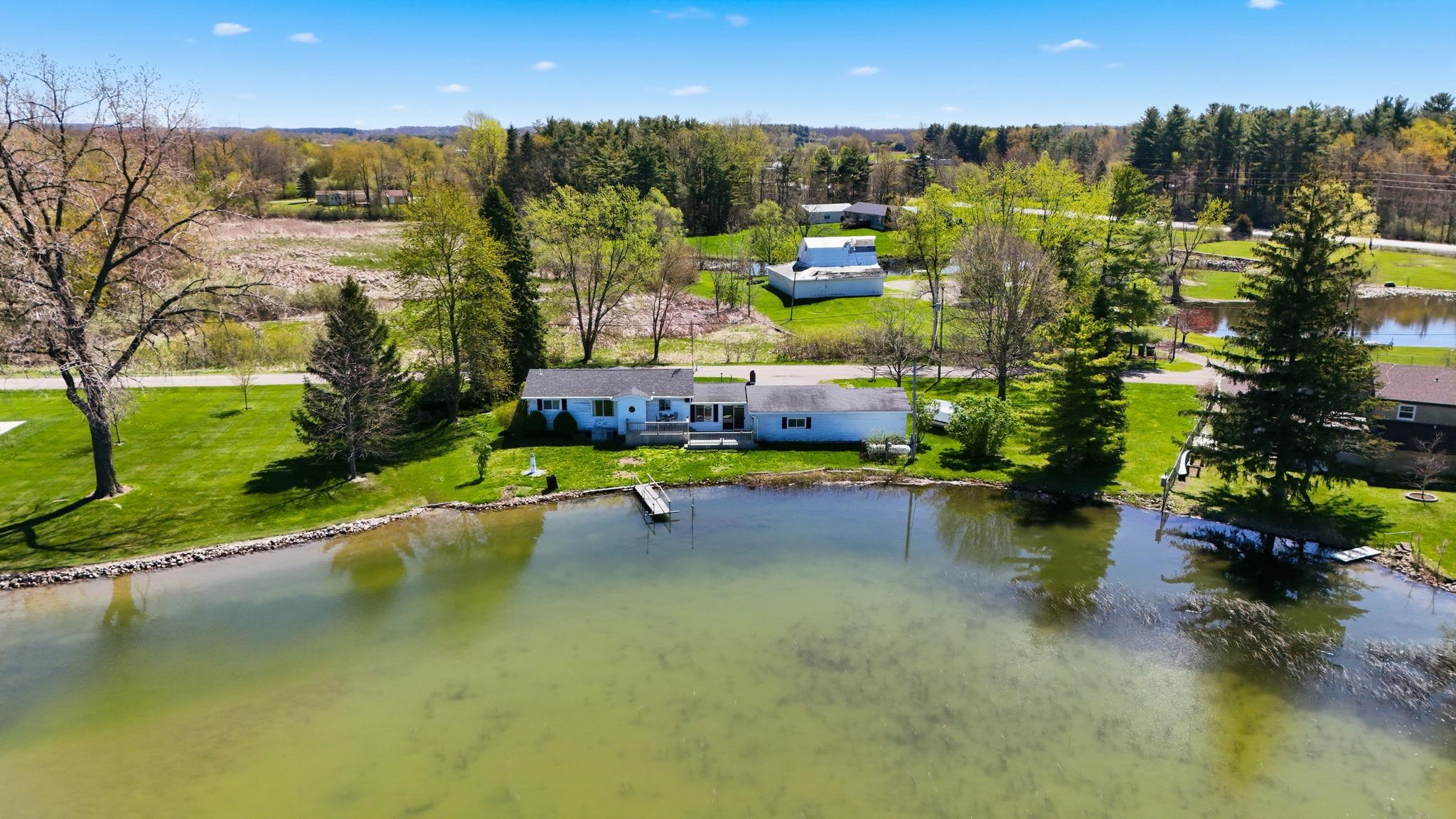 Lakefront property featuring a private dock, expansive green lawn, mature trees, and a detached garage