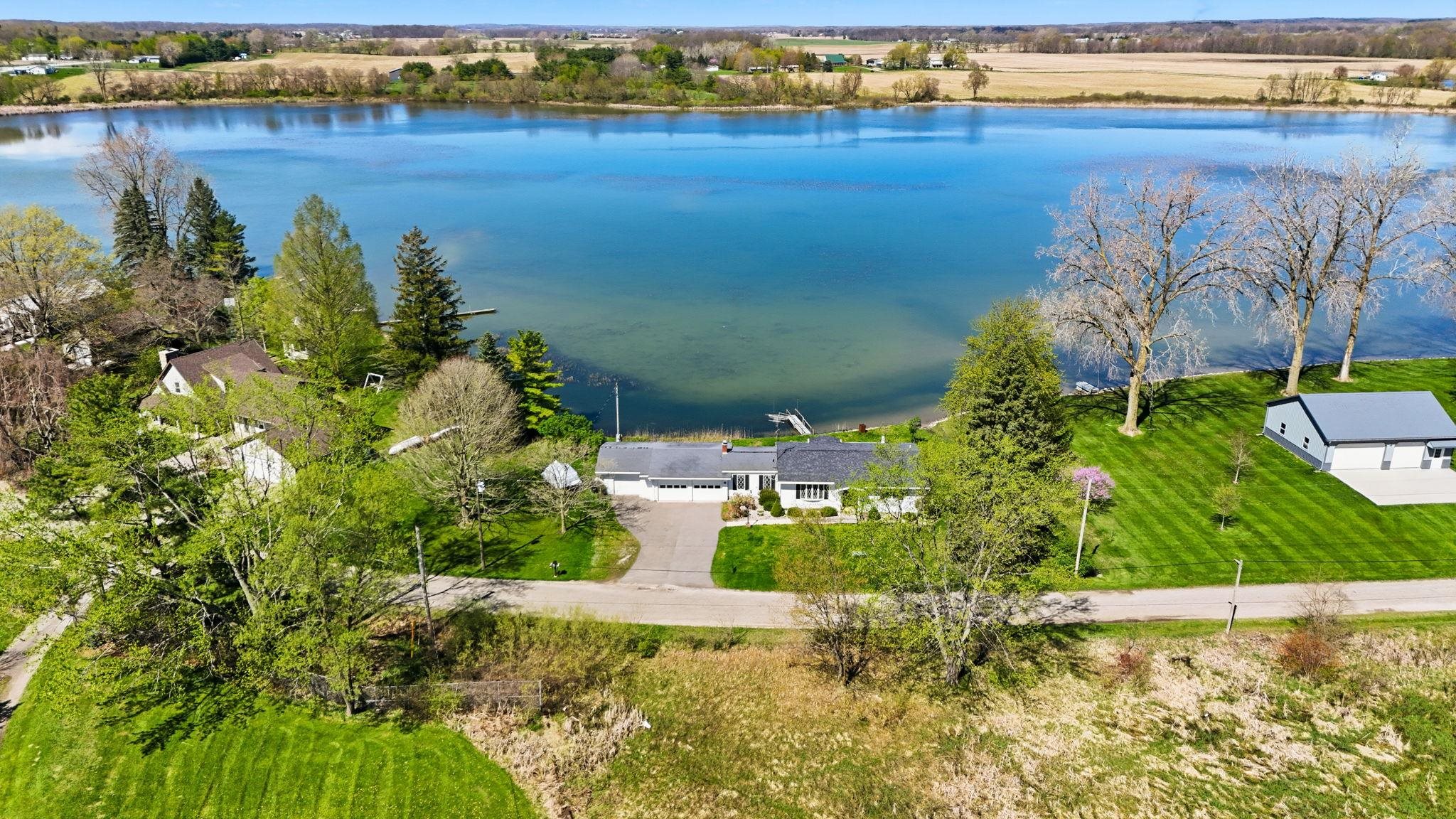Waterfront property featuring a single-story residence with a white exterior, attached garage, and a private dock extending into the lake