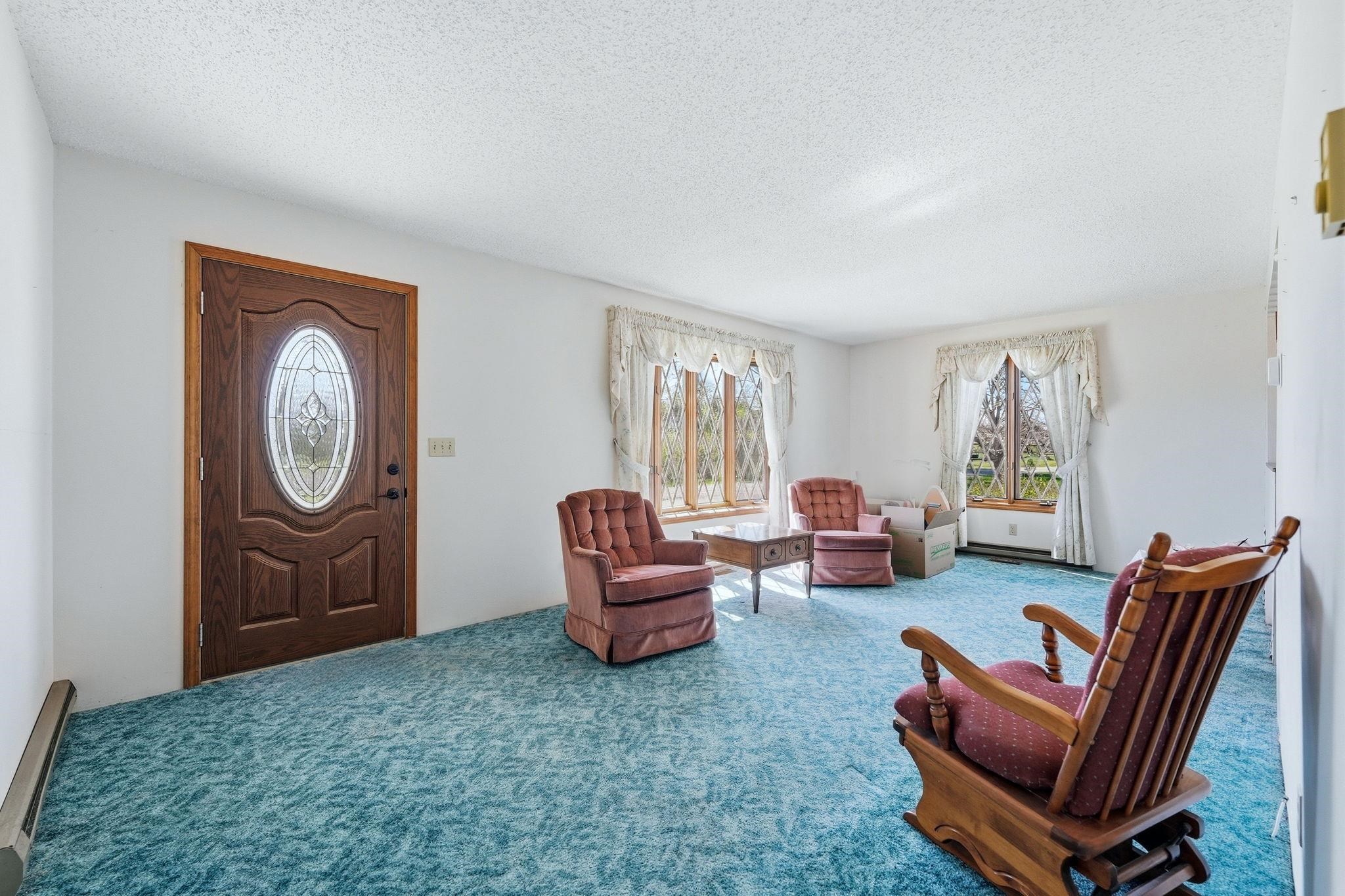 Entryway and living area featuring a decorative wood-finish entry door with an oval glass insert, textured ceilings, light-colored walls, and multiple windows