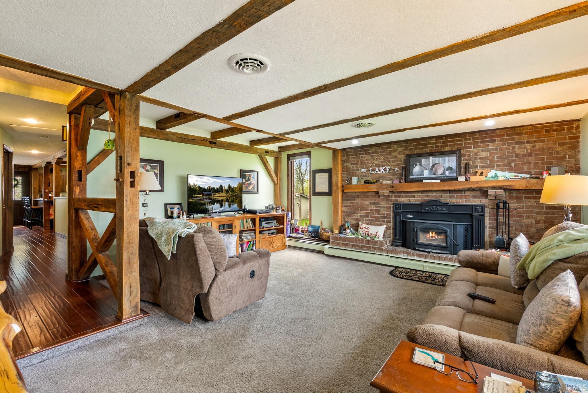 Carpeted living room featuring brick wall, beam ceiling, a textured ceiling, and a brick fireplace