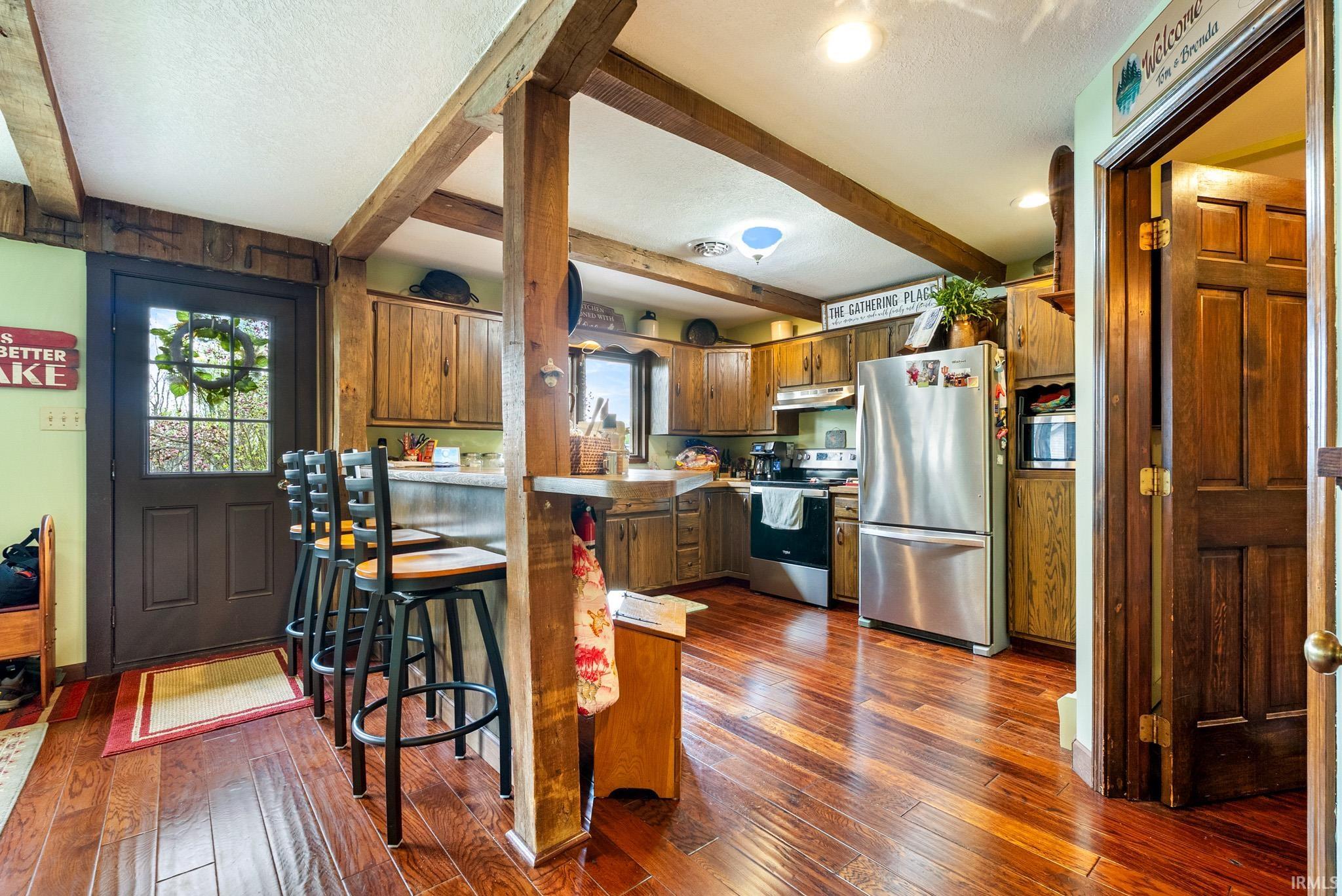 Kitchen featuring light countertops, stainless steel appliances, wood finish cabinets, a textured ceiling, and dark wood-style floors