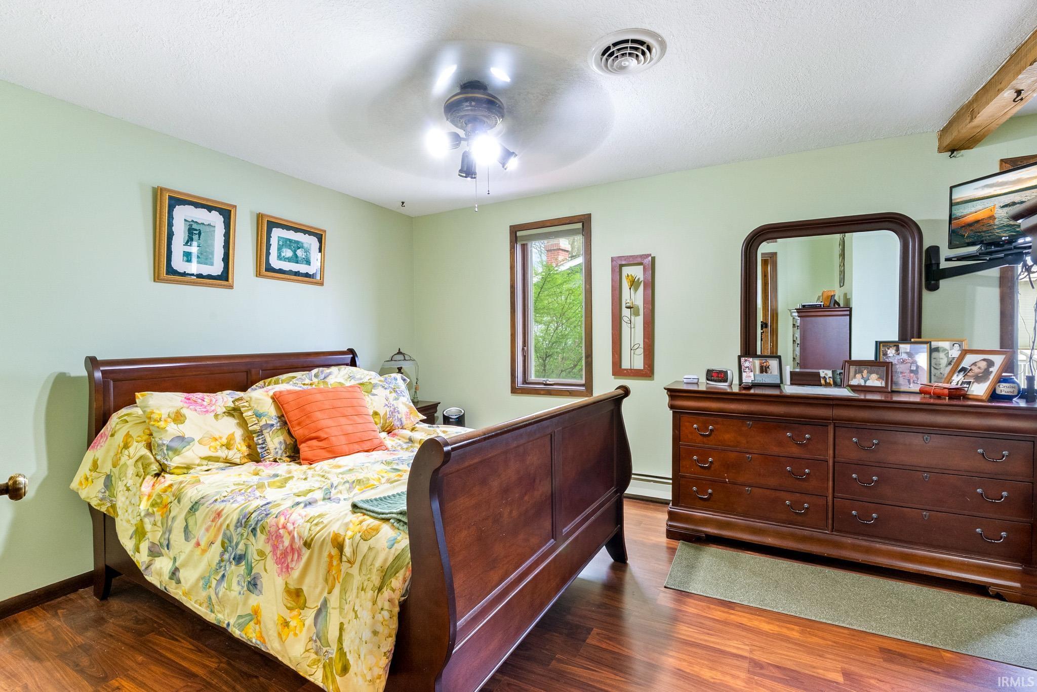Bedroom with wood finished floors, a ceiling fan, and baseboard heating