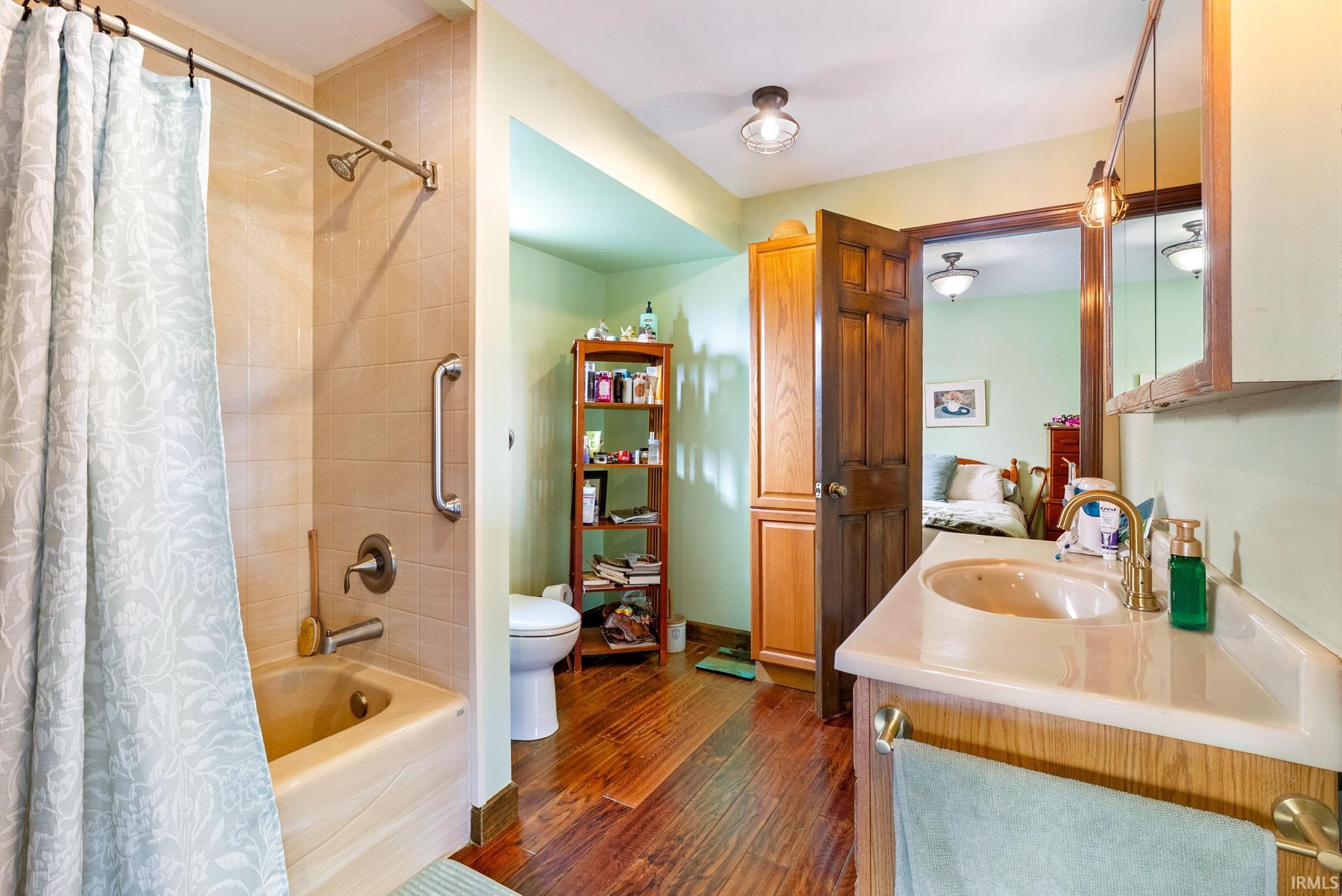 Ensuite bathroom with vanity, shower / bath combination with curtain, and dark wood-style floors