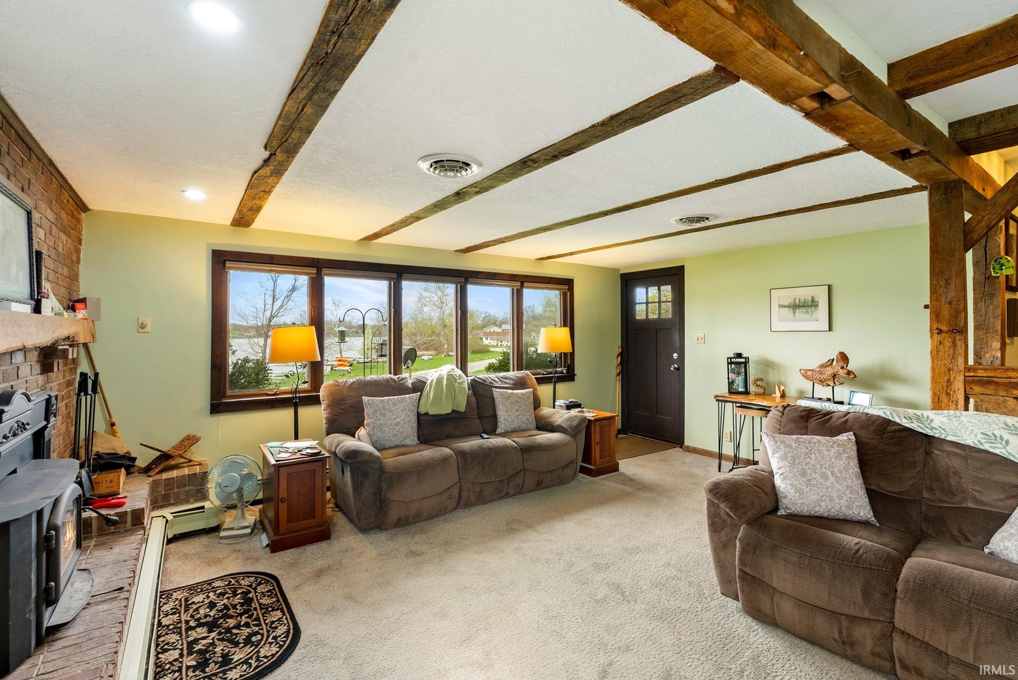 Living room with beam ceiling, light colored carpet, a fireplace, and brick wall