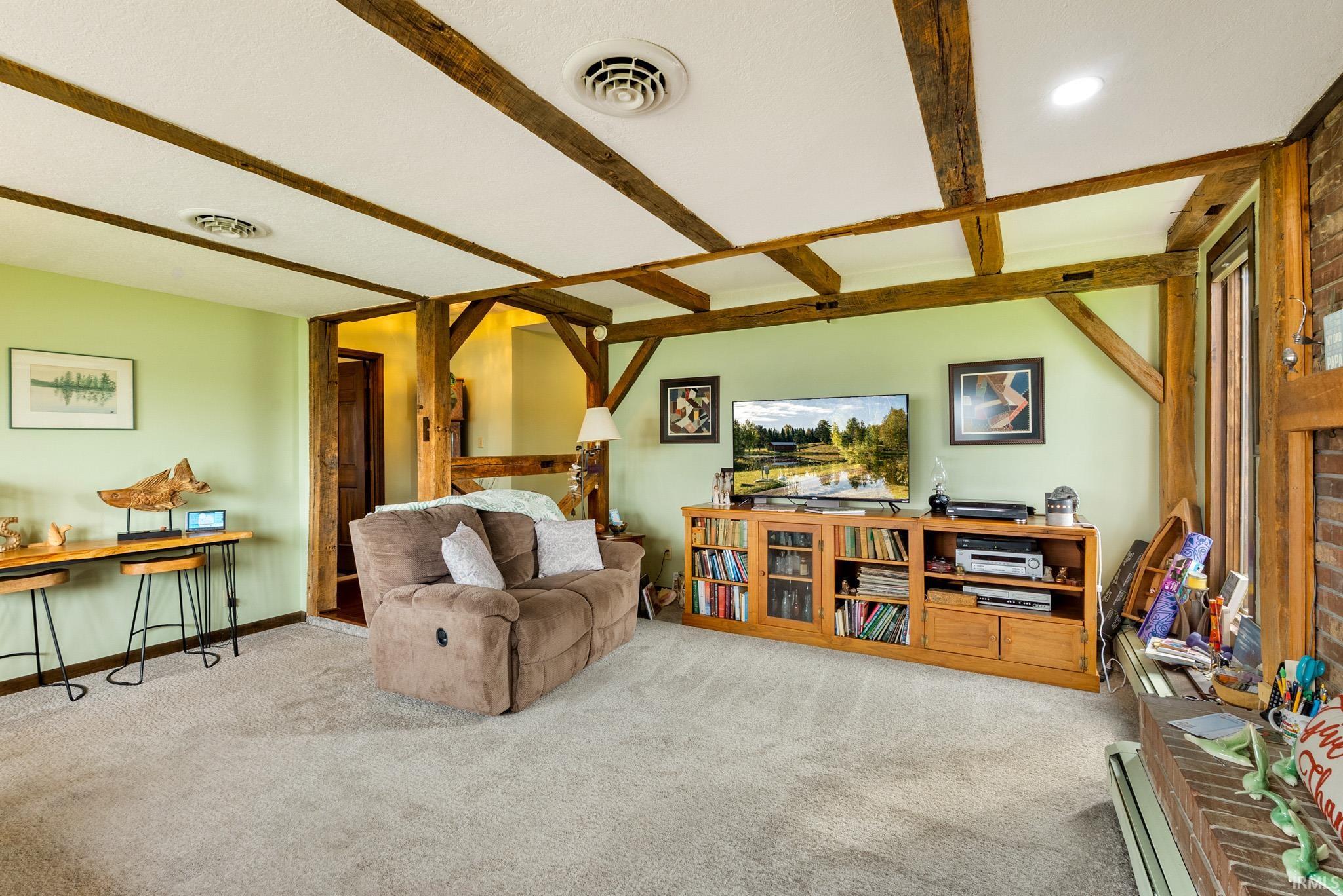 Living room featuring a baseboard heating unit, light colored carpet, beam ceiling, and brick wall