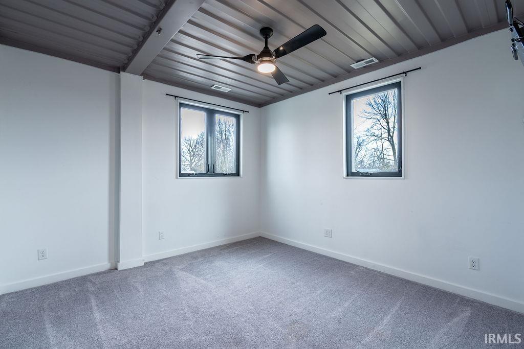 Empty room featuring plenty of natural light, carpet flooring, and a ceiling fan
