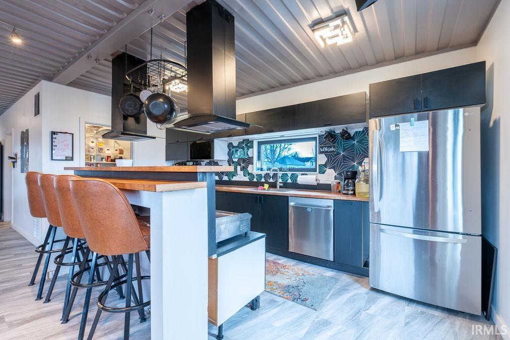 Kitchen featuring stainless steel appliances, island exhaust hood, ventilation hood, and a kitchen bar