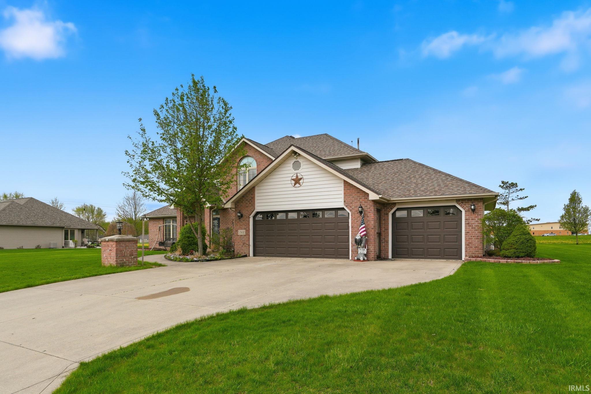 Traditional home featuring a garage, brick siding, a front lawn, driveway, and roof with shingles