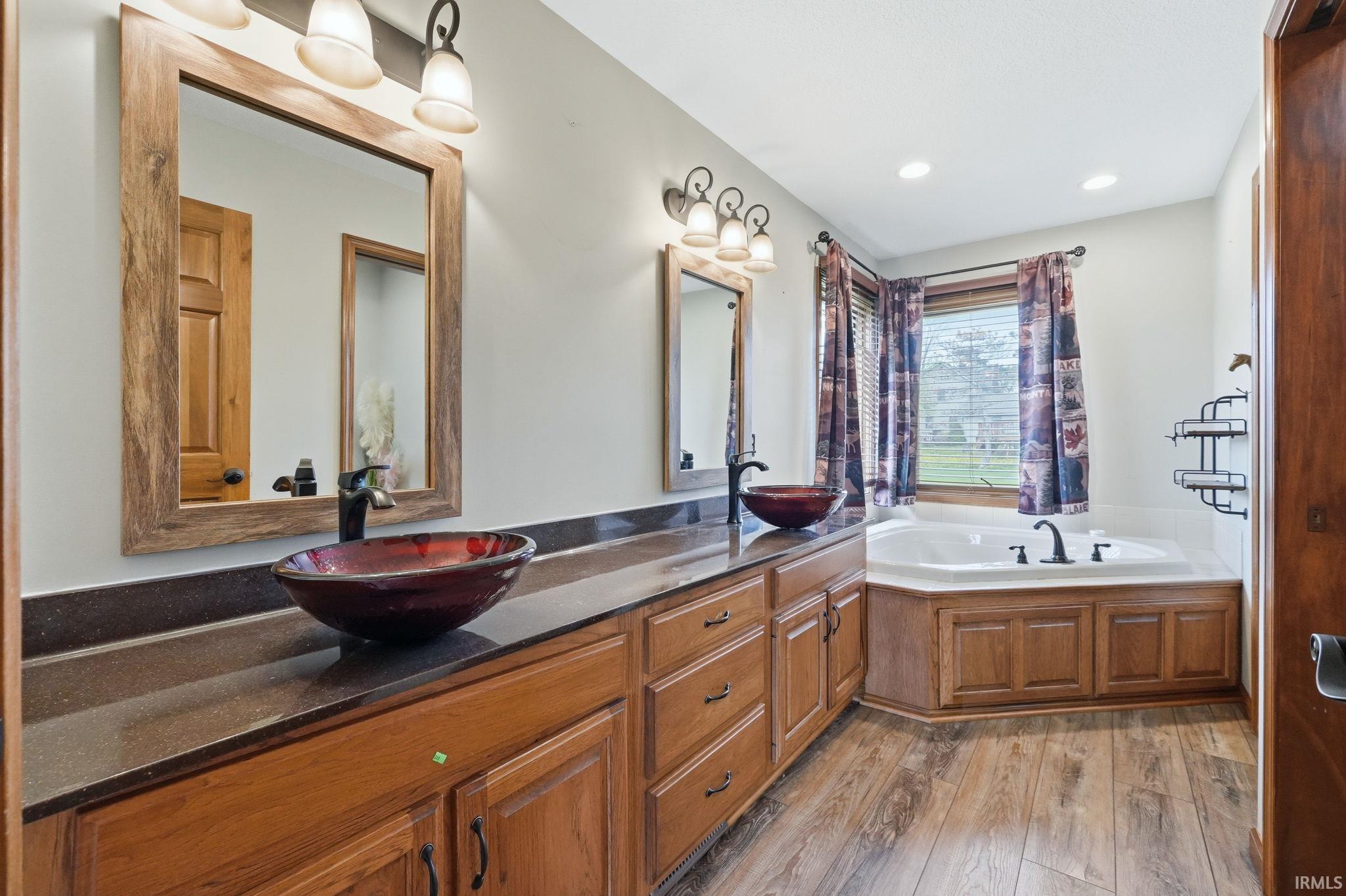Bathroom with double vanity, a garden tub, light wood-type flooring, and recessed lighting