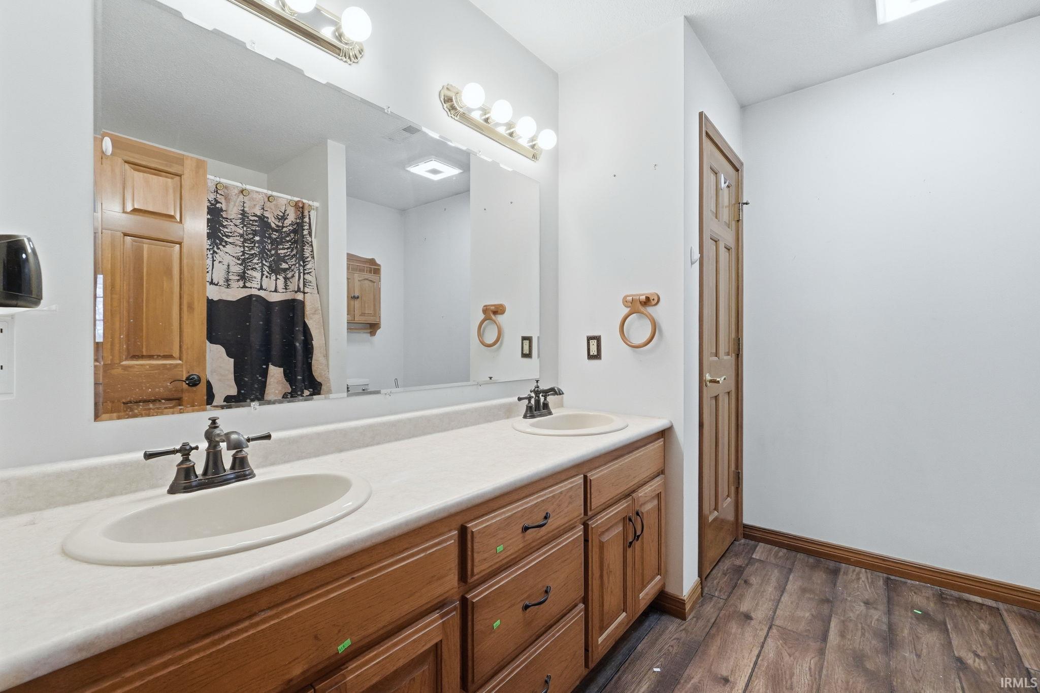 Bathroom with double vanity, a shower with shower curtain, and dark wood-style floors