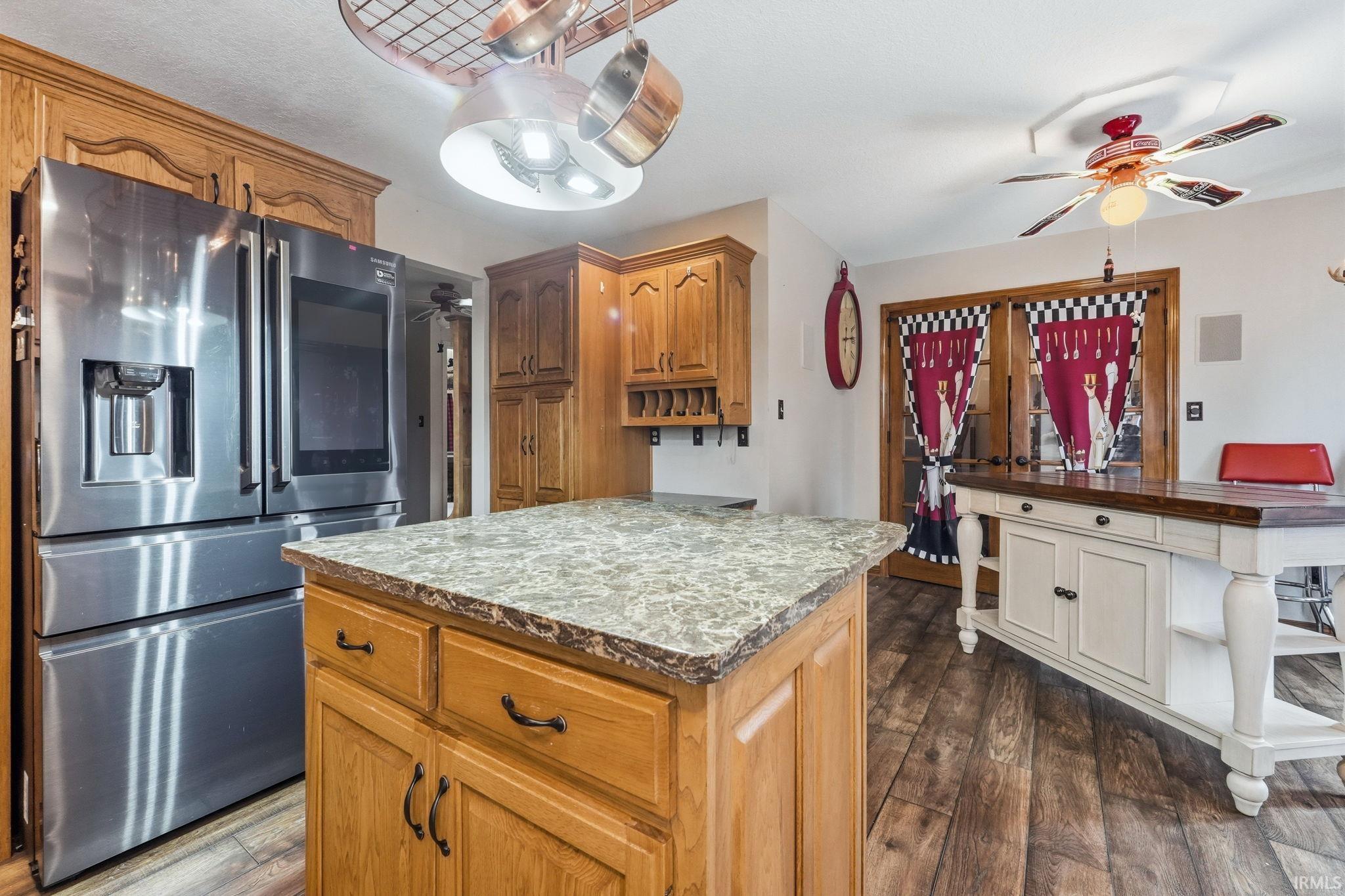 Kitchen with stainless steel fridge, ceiling fan, a kitchen island, and dark wood-type flooring