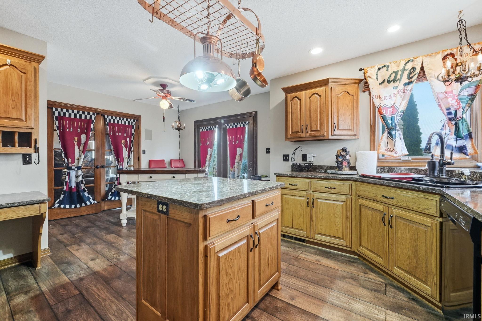 Kitchen featuring a kitchen island, dark wood finished floors, dishwasher, ceiling fan, and dark stone counters