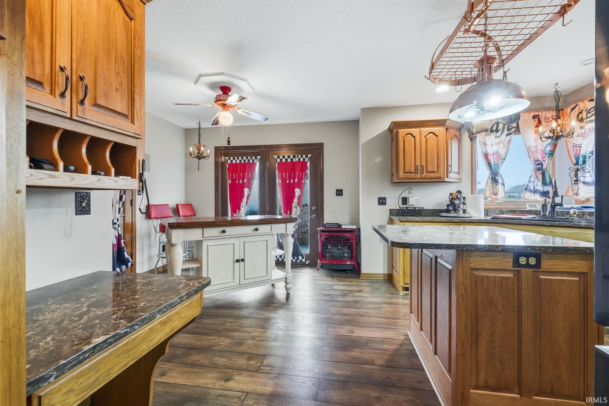 Kitchen with wood finish cabinets, suspended lighting, dark stone countertops, and dark wood finished floors