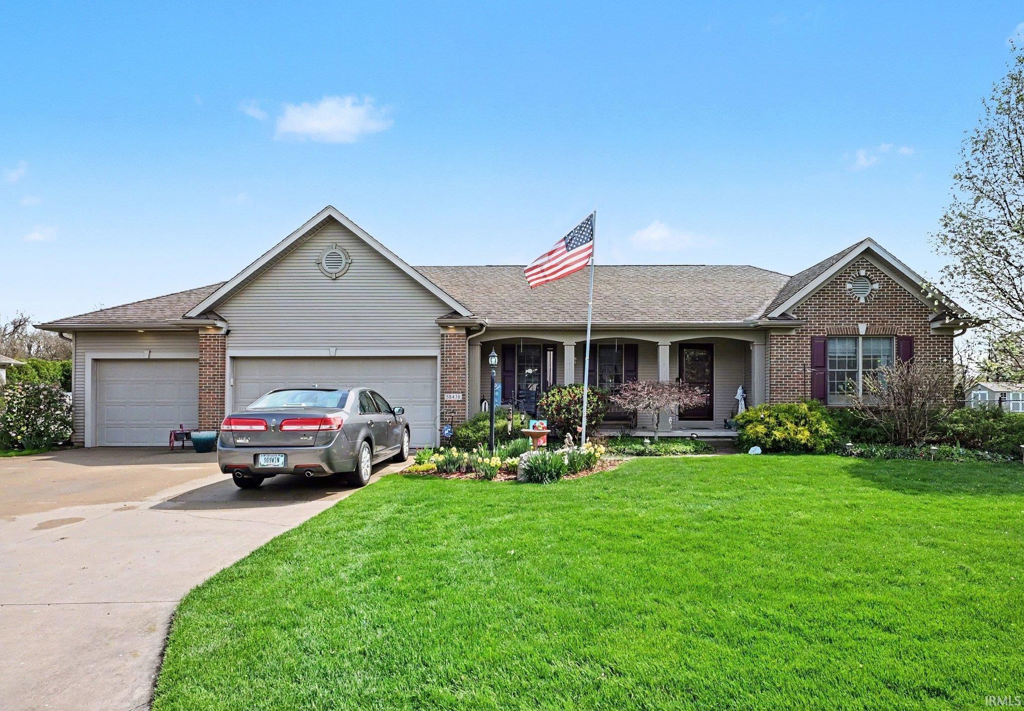 Ranch-style home featuring brick siding, covered porch, a garage, driveway, and roof with shingles
