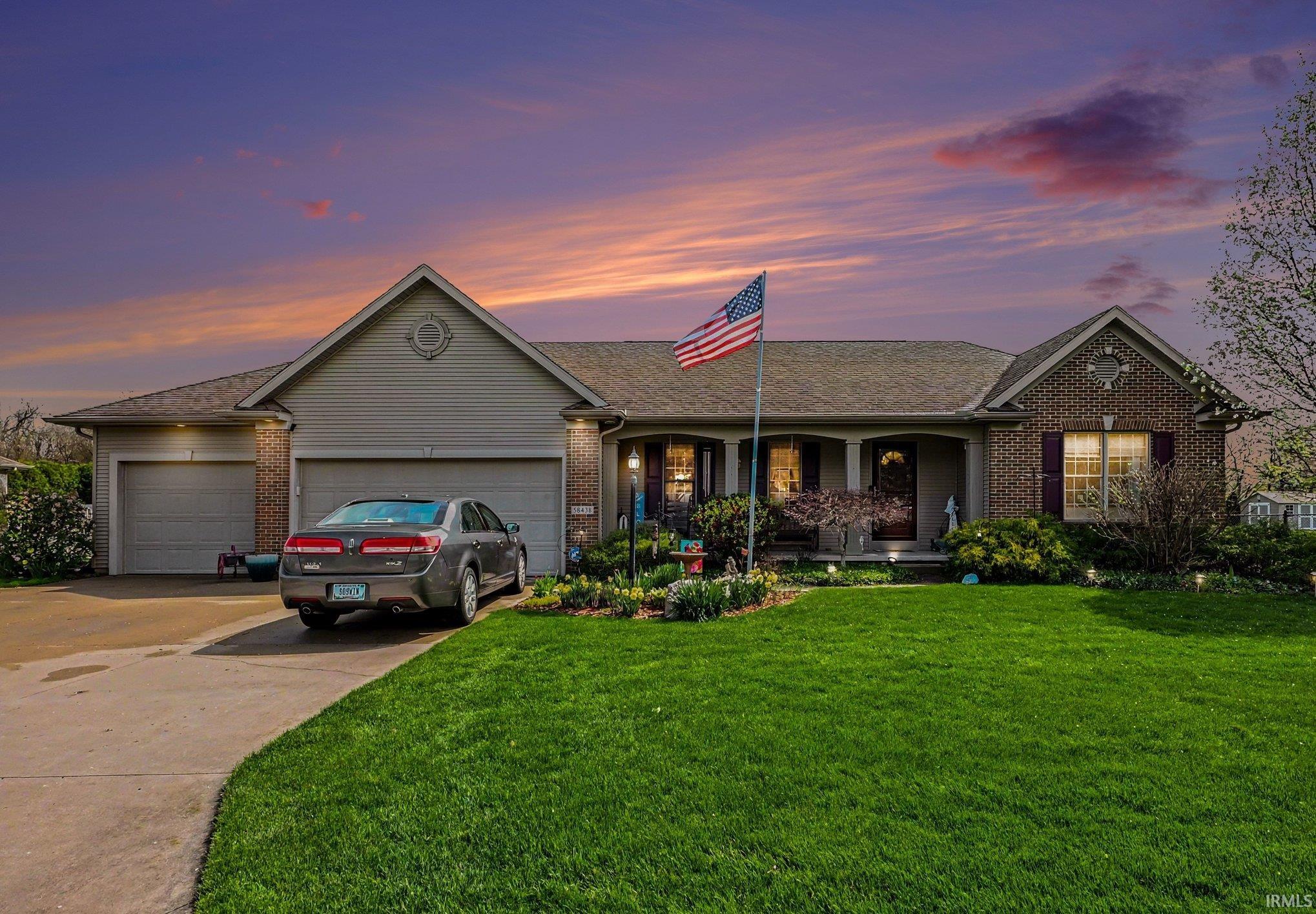 Single story home with brick siding, covered porch, a garage, concrete driveway, and a front lawn