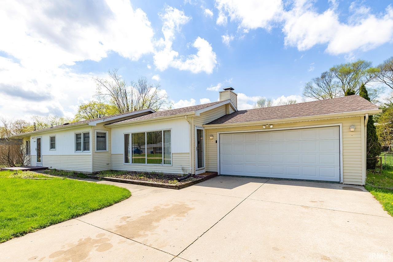 Ranch-style home featuring a front lawn, concrete driveway, an attached garage, a chimney, and roof with shingles