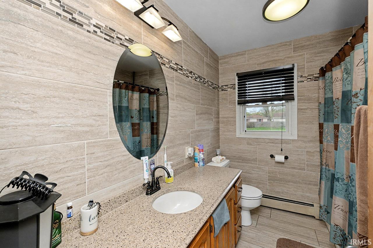 Bathroom featuring tile walls, baseboard heating, vanity, and a shower with curtain