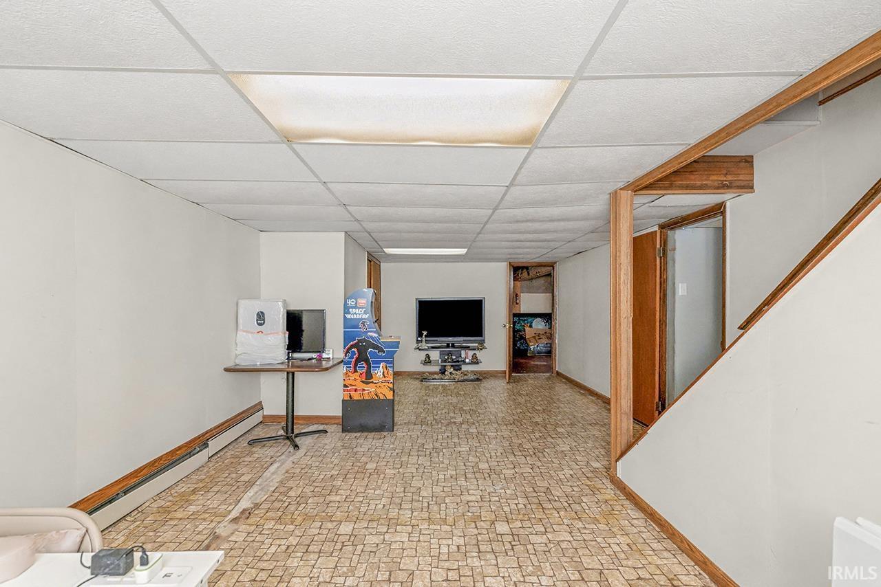 Finished below grade area with a drop ceiling, a baseboard radiator, and light floors