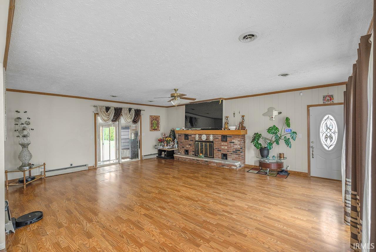 Living room featuring light wood finished floors, ornamental molding, a ceiling fan, a textured ceiling, and a brick fireplace