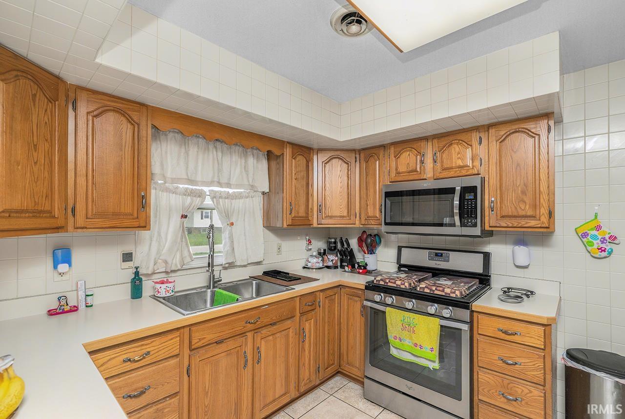 Kitchen featuring light countertops, stainless steel appliances, wood finish cabinets, light tile patterned floors, and tasteful backsplash
