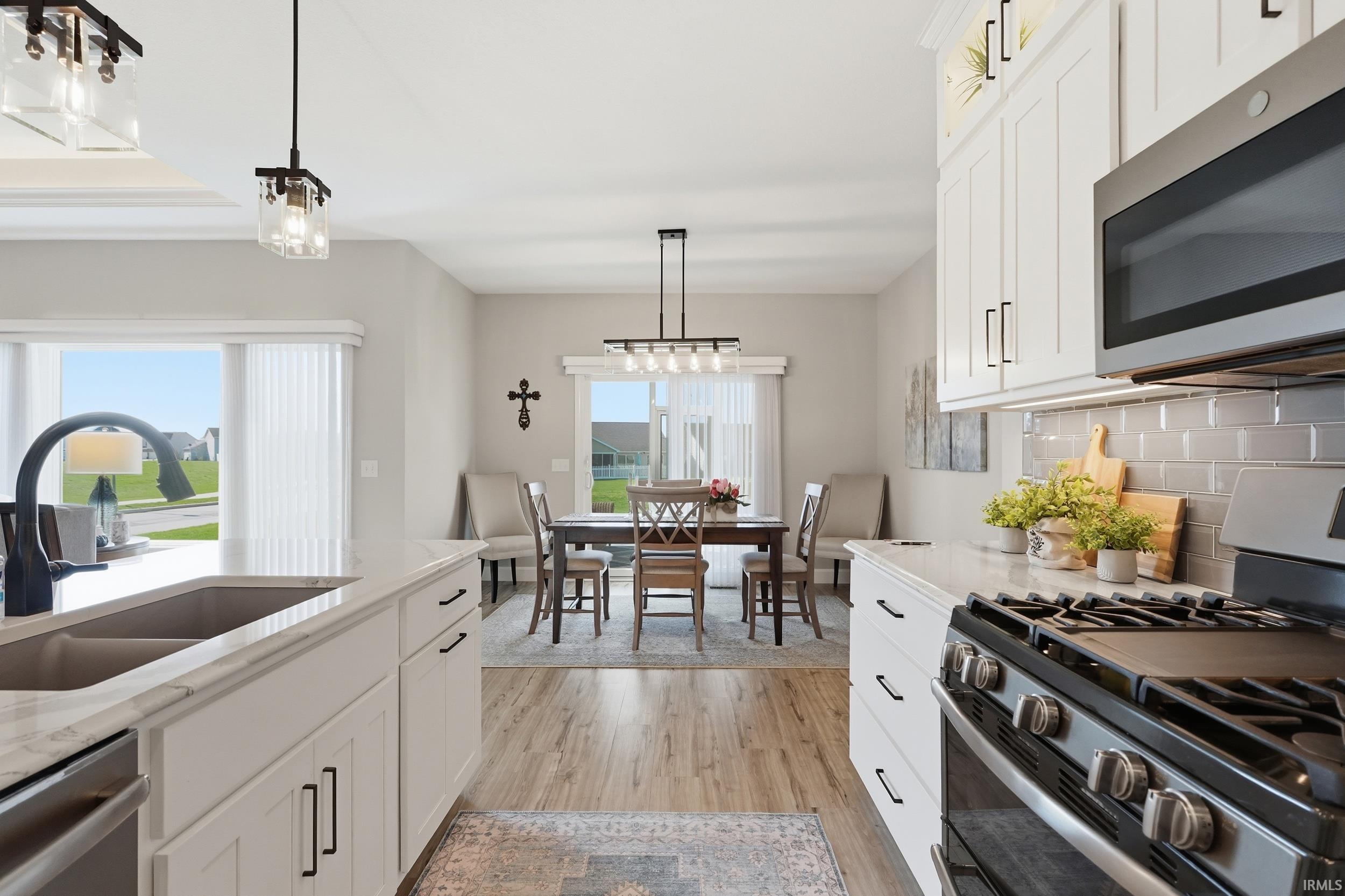 Kitchen featuring stainless steel appliances, white cabinets, light wood-type flooring, and light stone counters