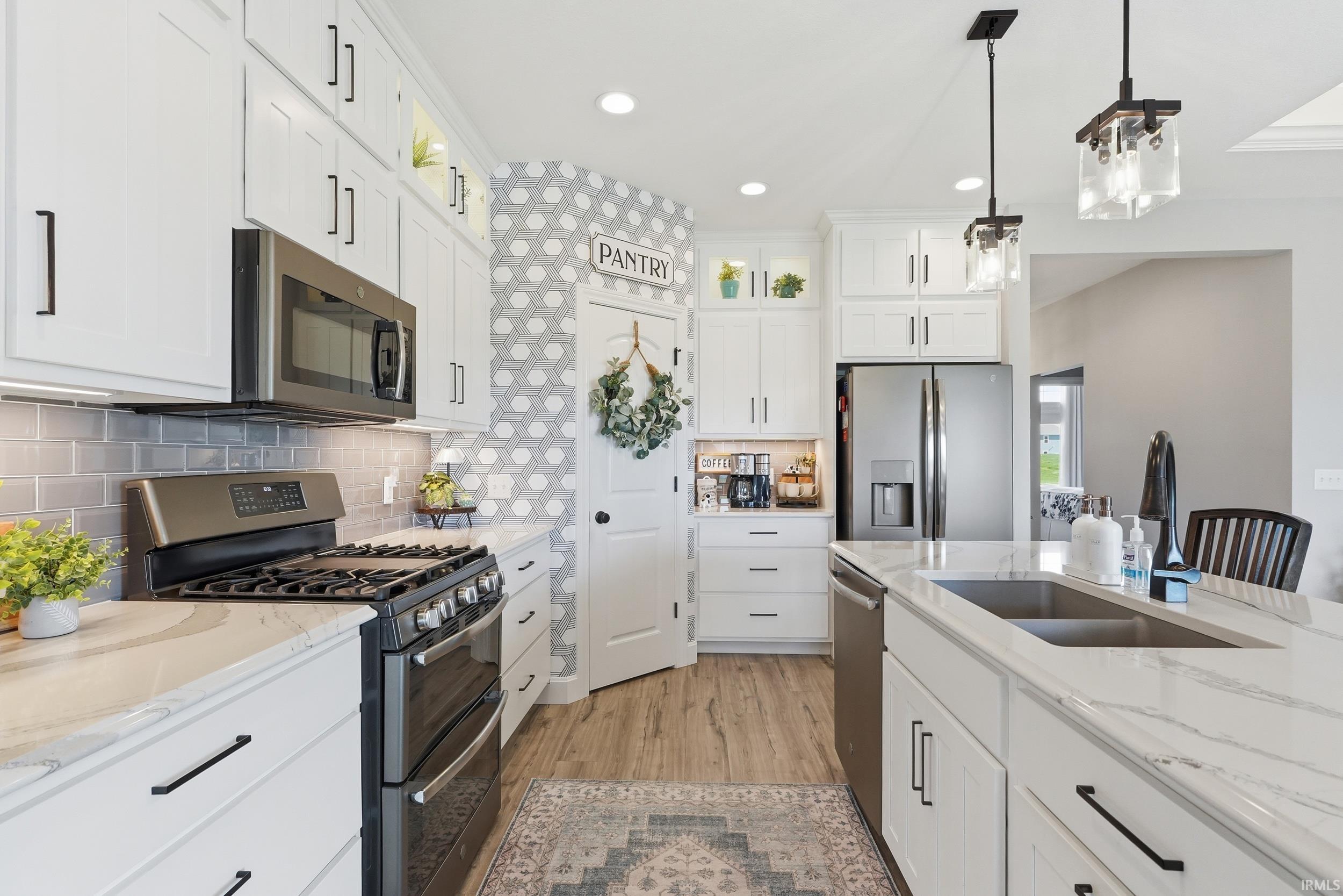 Kitchen featuring stainless steel appliances, white cabinets, and light stone countertops
