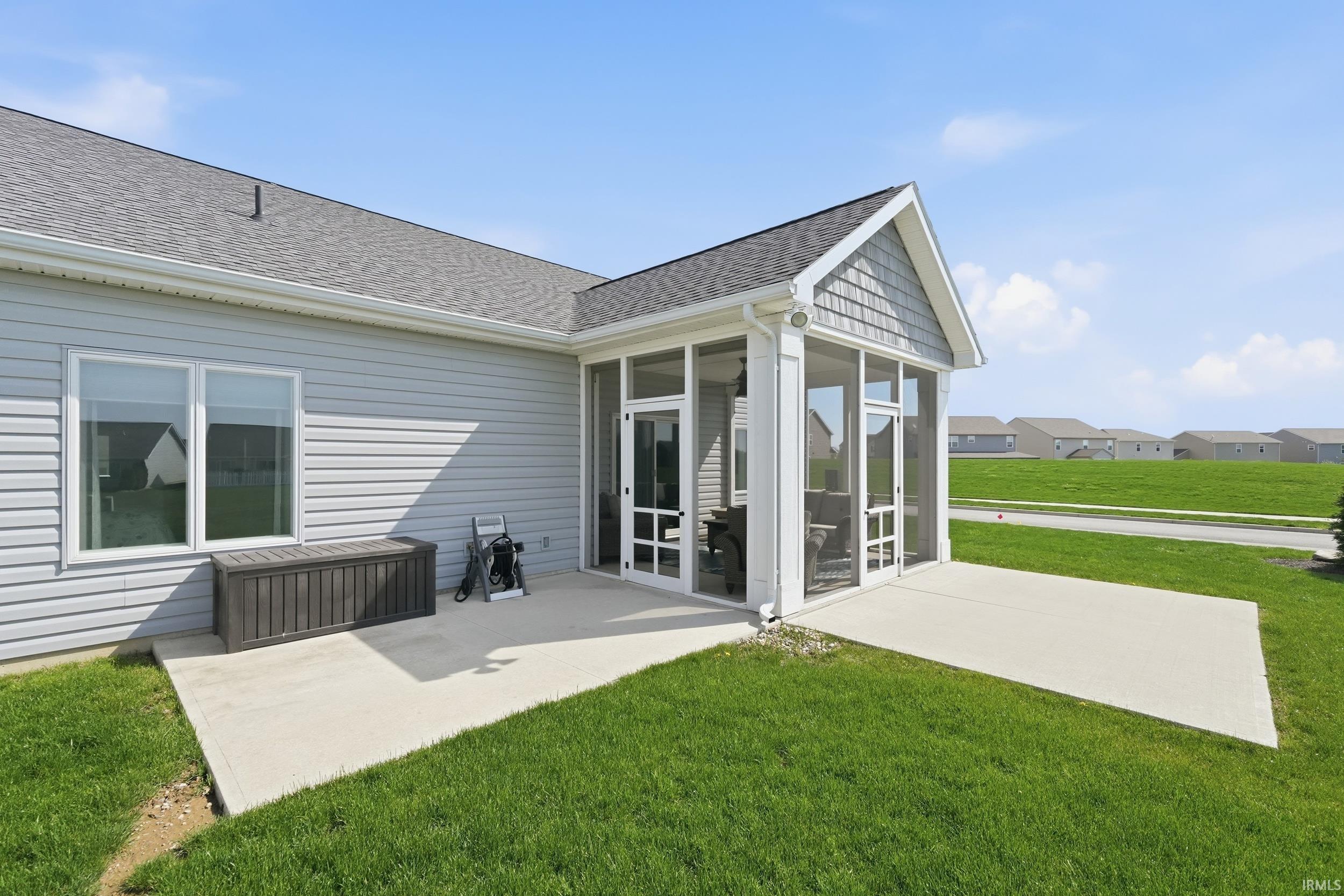 Rear view of house with a patio area, a sunroom, a lawn, roof with shingles, and a residential view