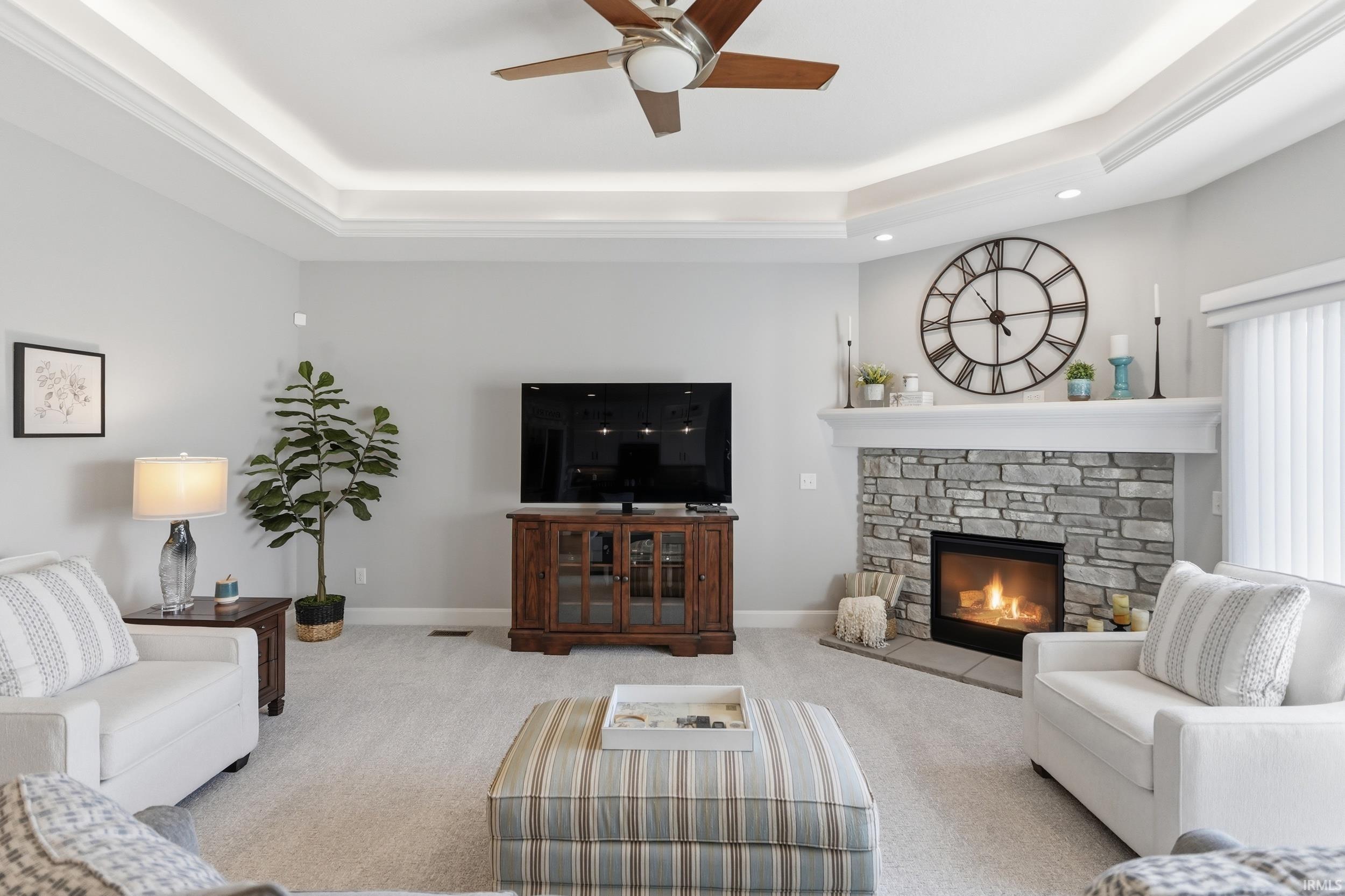Carpeted living room featuring a tray ceiling, ceiling fan, a fireplace, and recessed lighting