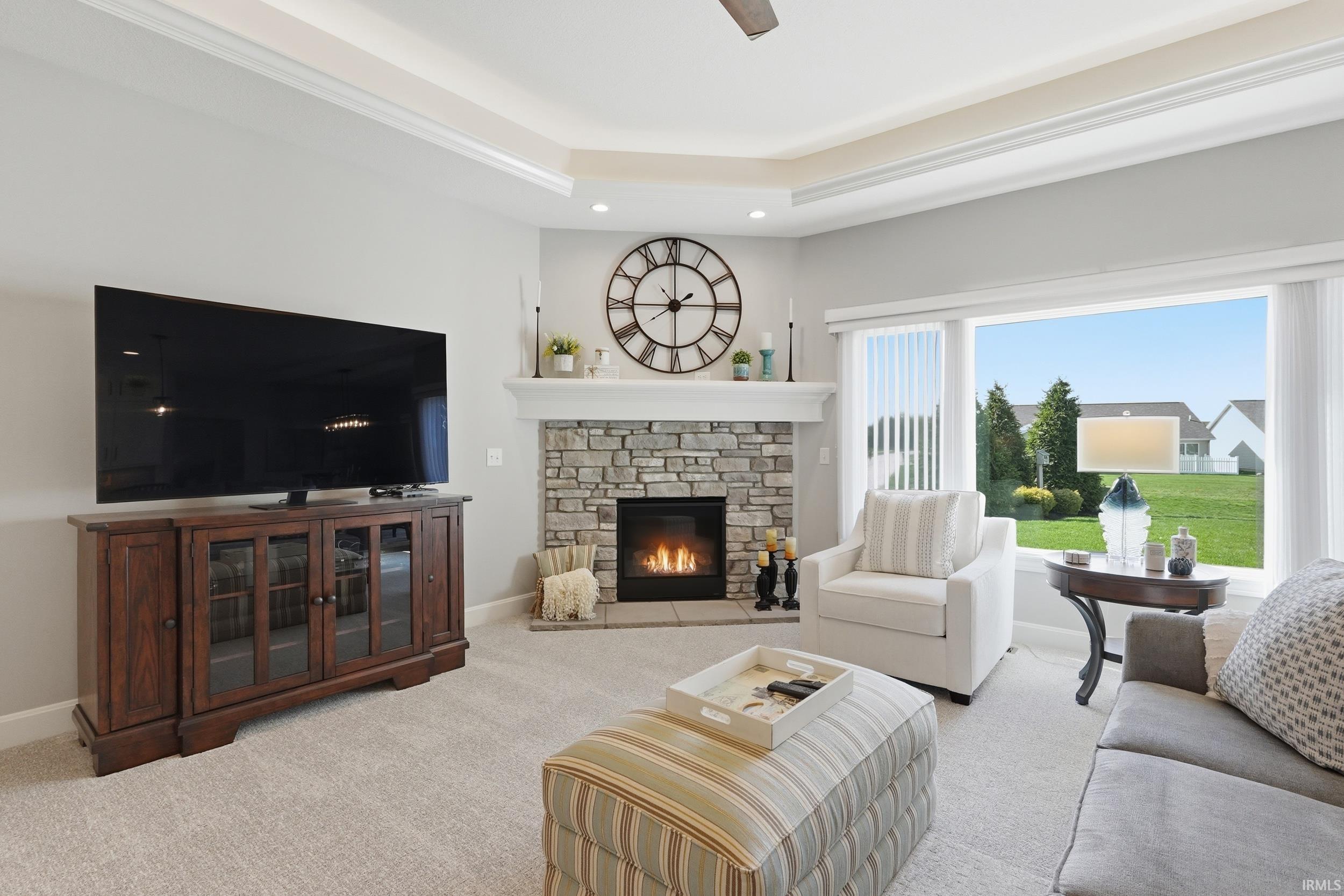 Carpeted living room featuring a stone fireplace, recessed lighting, a ceiling fan, and a tray ceiling