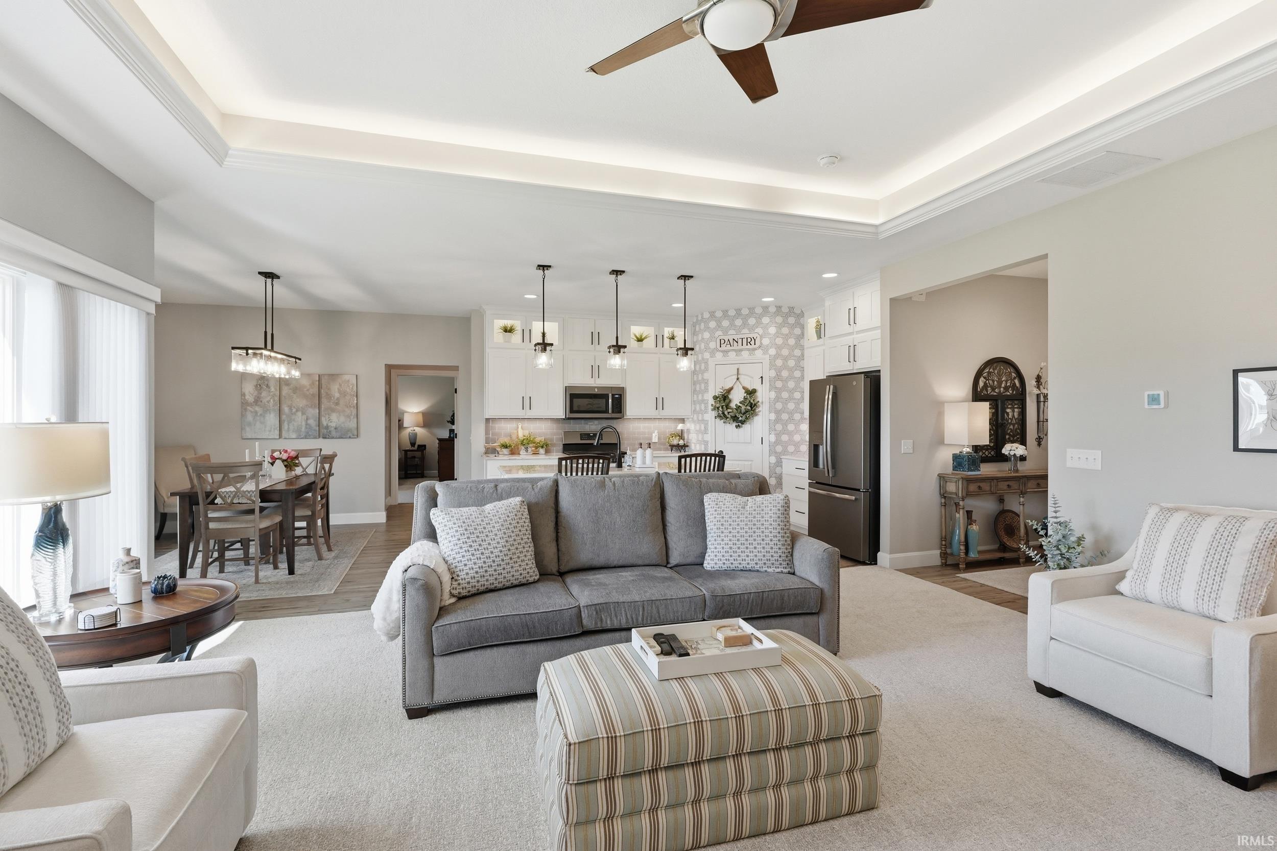 Living room with a raised ceiling, a ceiling fan, and a chandelier