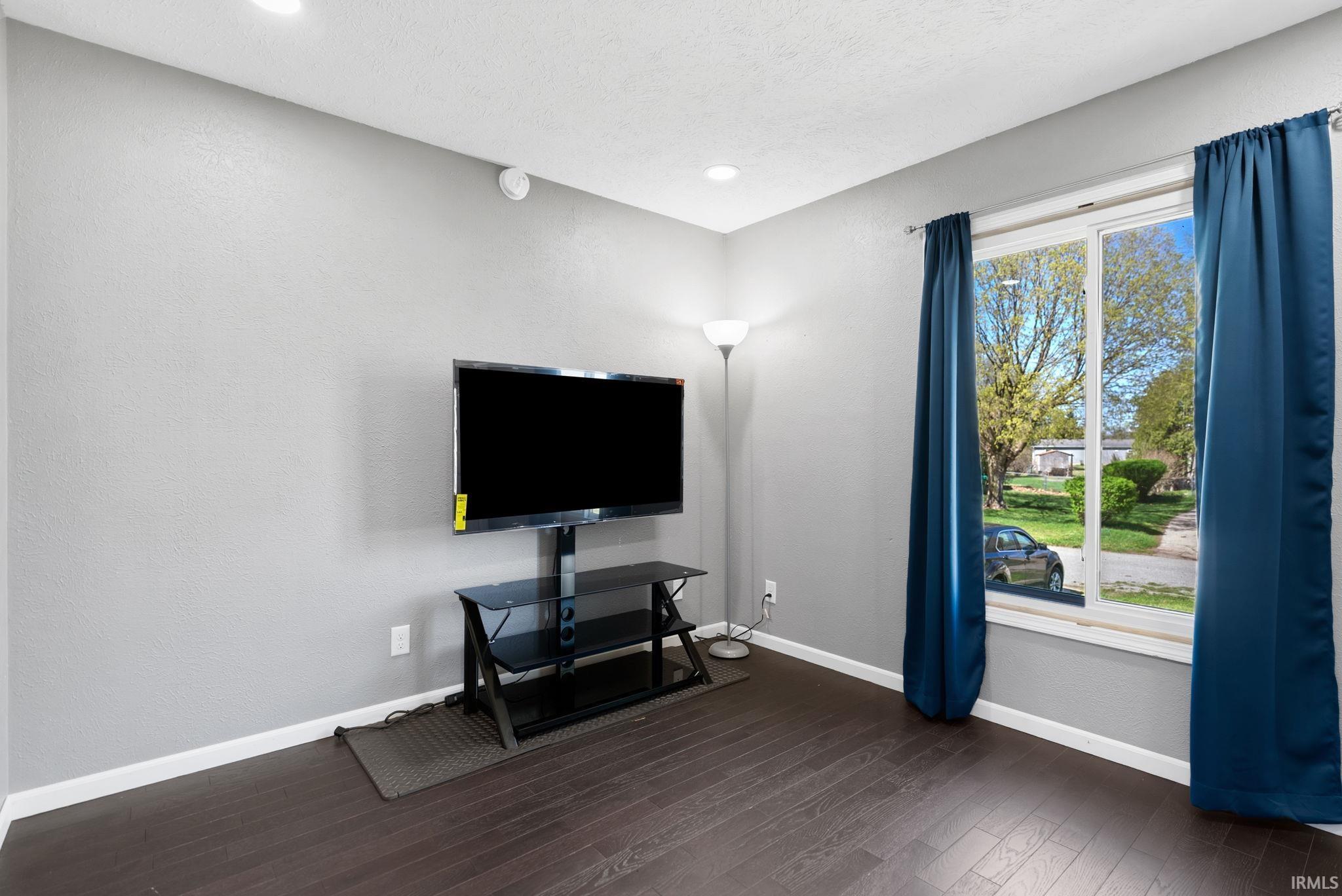 Living area featuring dark wood-style flooring and a textured wall