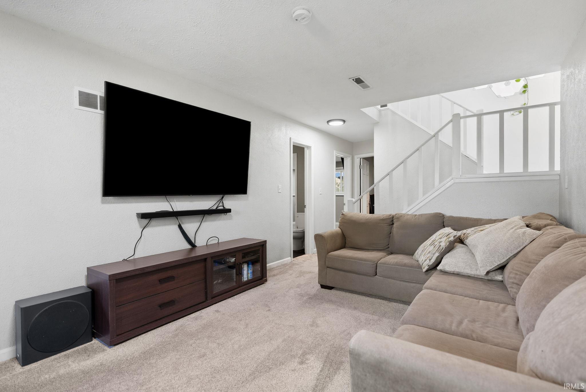 Carpeted living area with stairs and baseboards